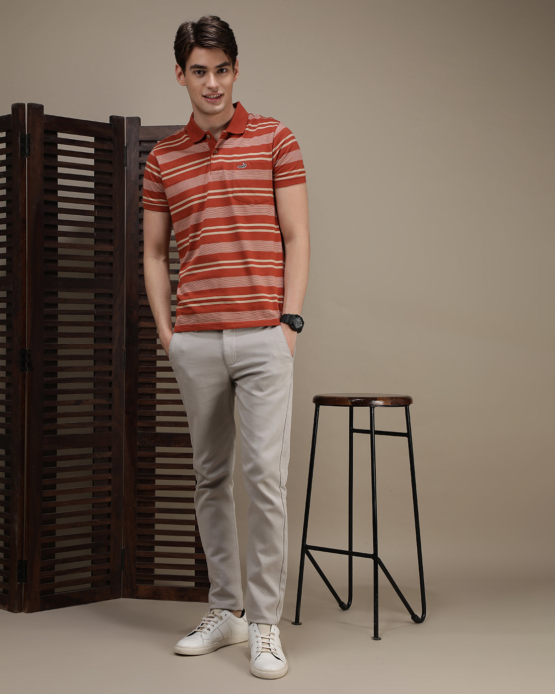 Man wearing a dusty orange striped polo t shirt with casual styling on a gray background
