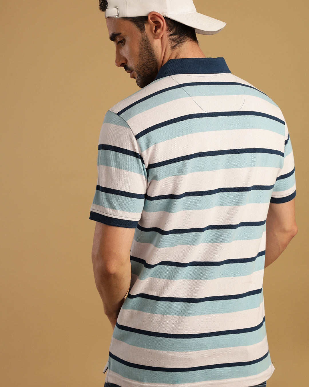Man wearing a white blue and white striped polo t shirt with casual styling on a gray background