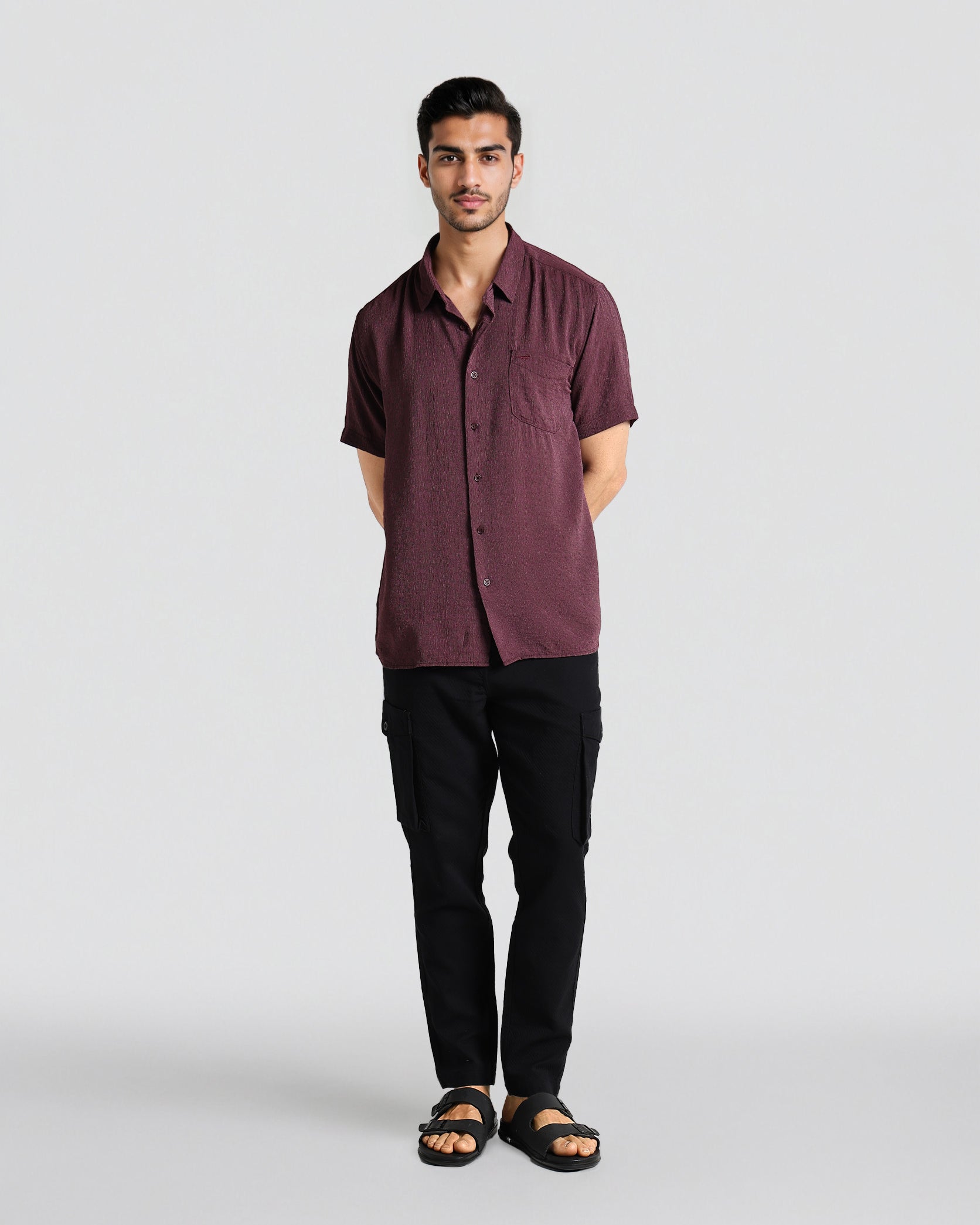 Man wearing a maroon shirt and black pants on a white background