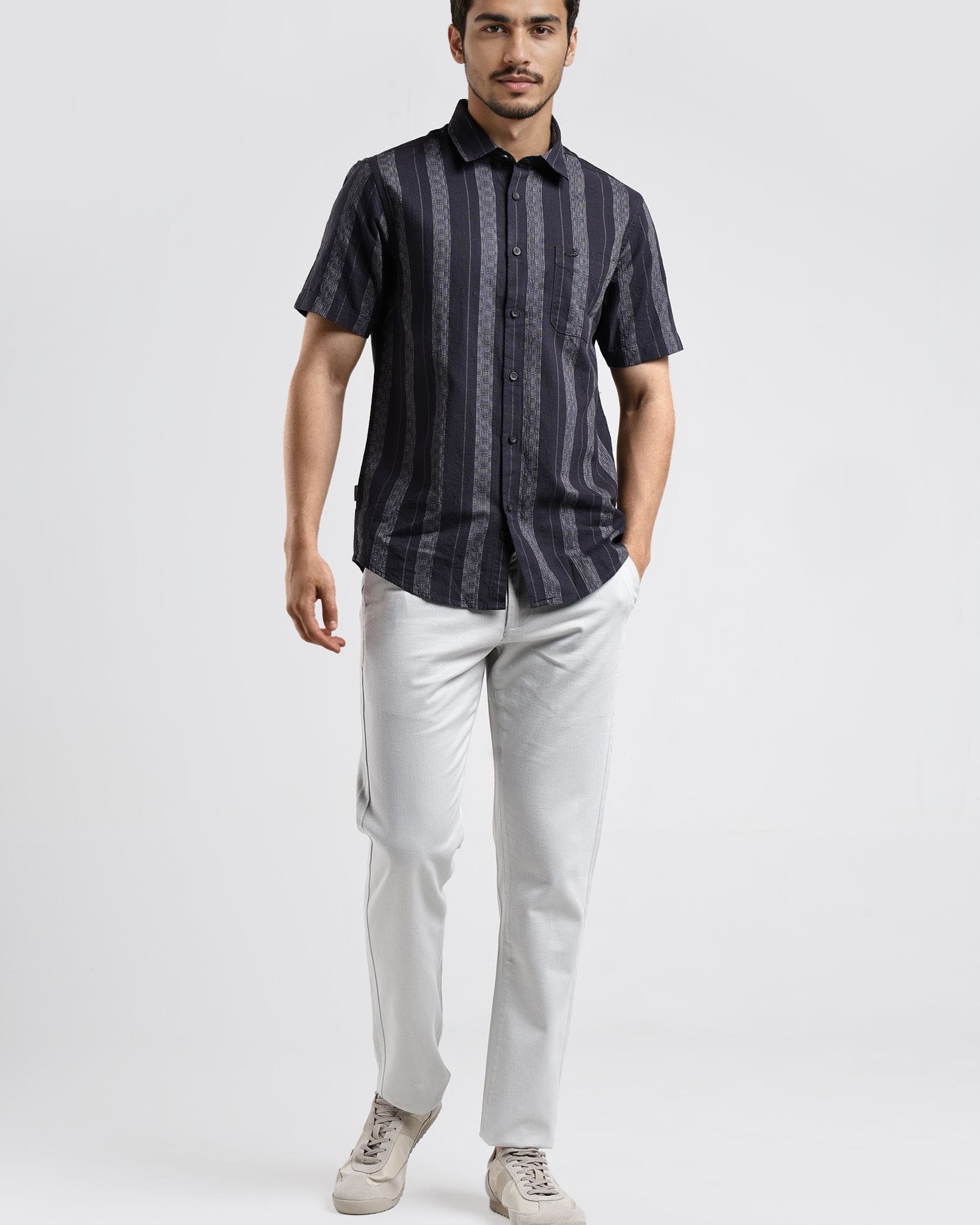 Man wearing a dark striped shirt and light pants on a white background