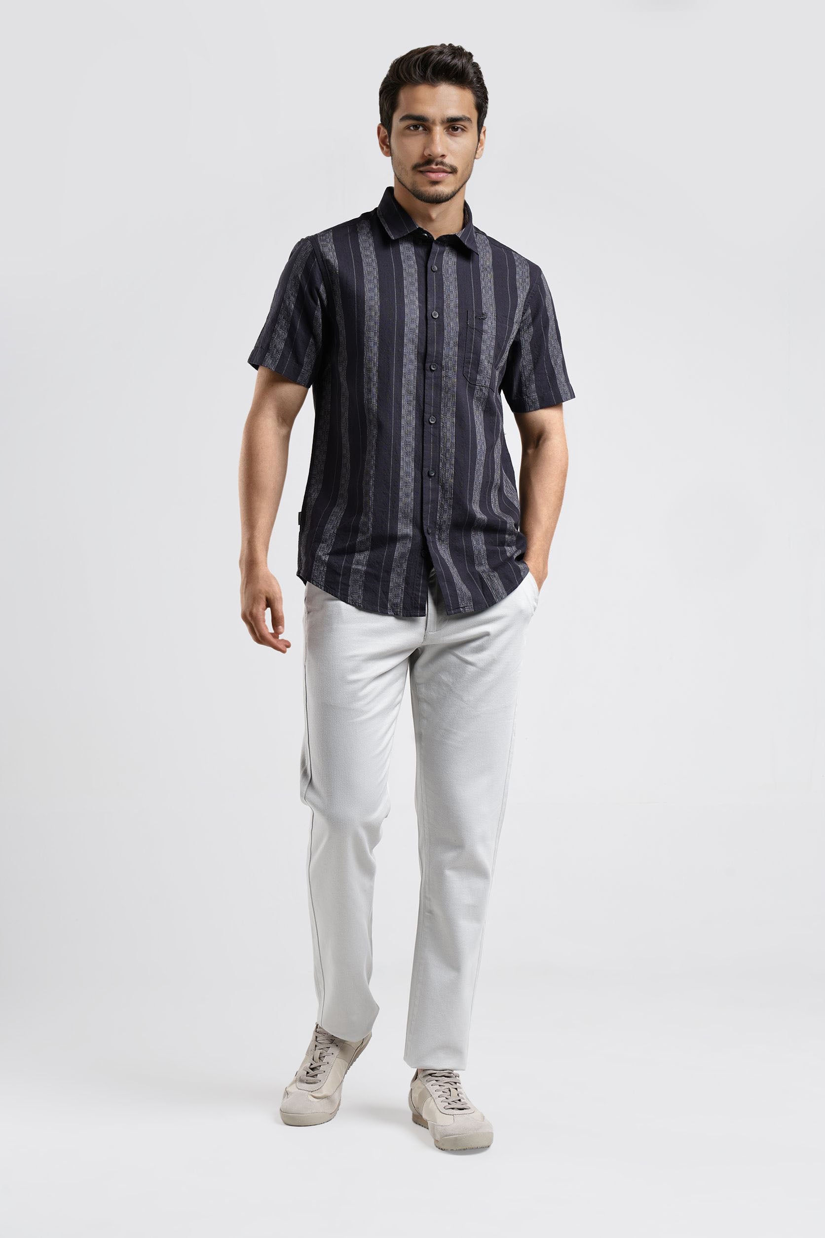 Man wearing a dark striped shirt and light pants on a white background