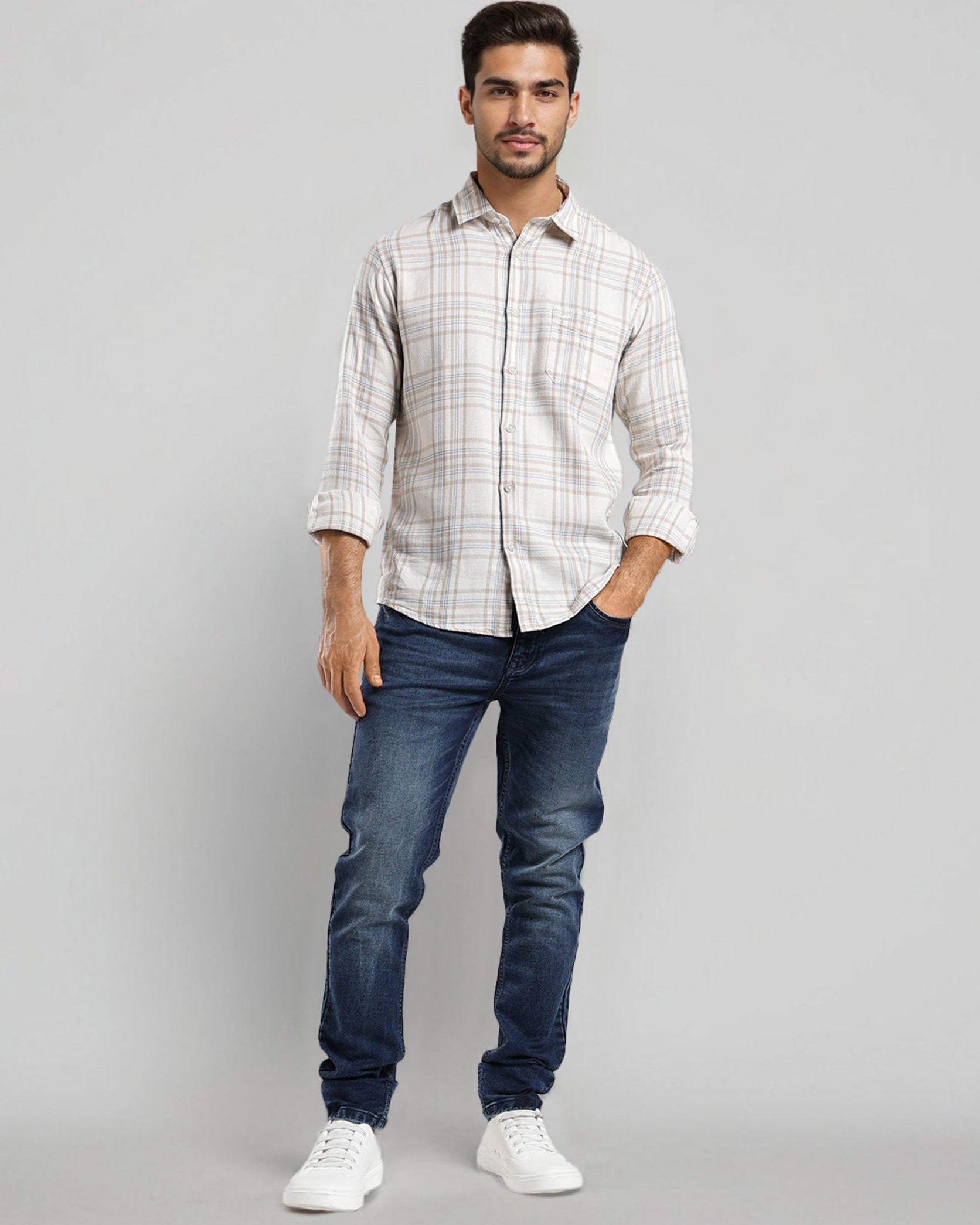Man wearing a checkered shirt, blue jeans, and white sneakers on a gray background