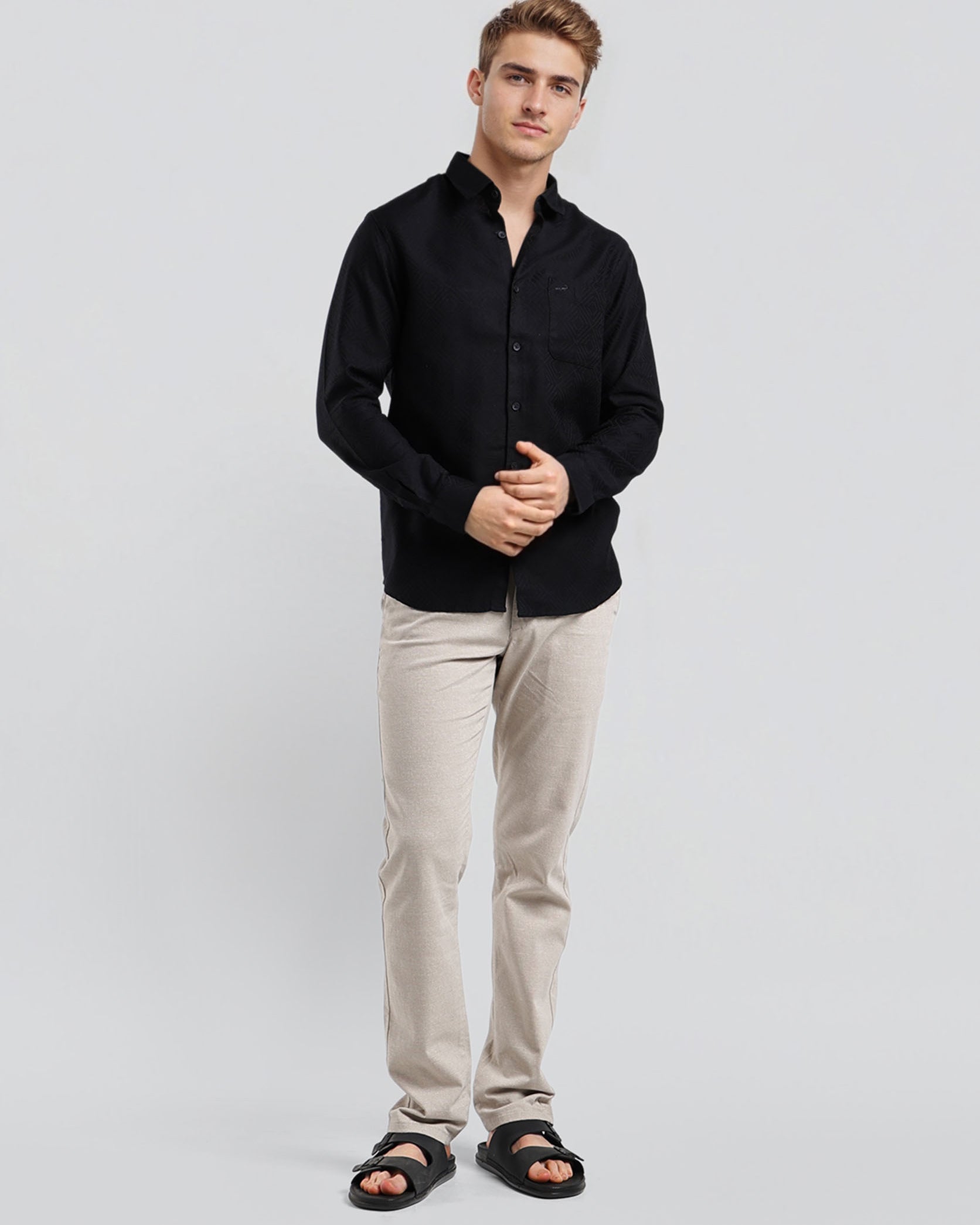 Man wearing a black shirt and beige pants on a light gray background