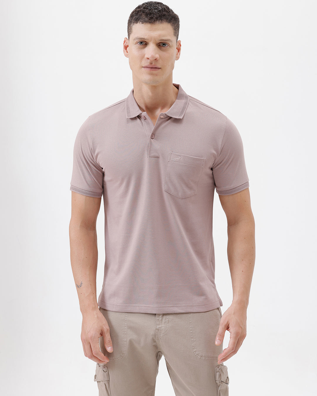 A man modeling a short-sleeve polo shirt in a dusty mauve-pink color, paired with khaki cargo pants and a baseball cap, against a plain light gray background.