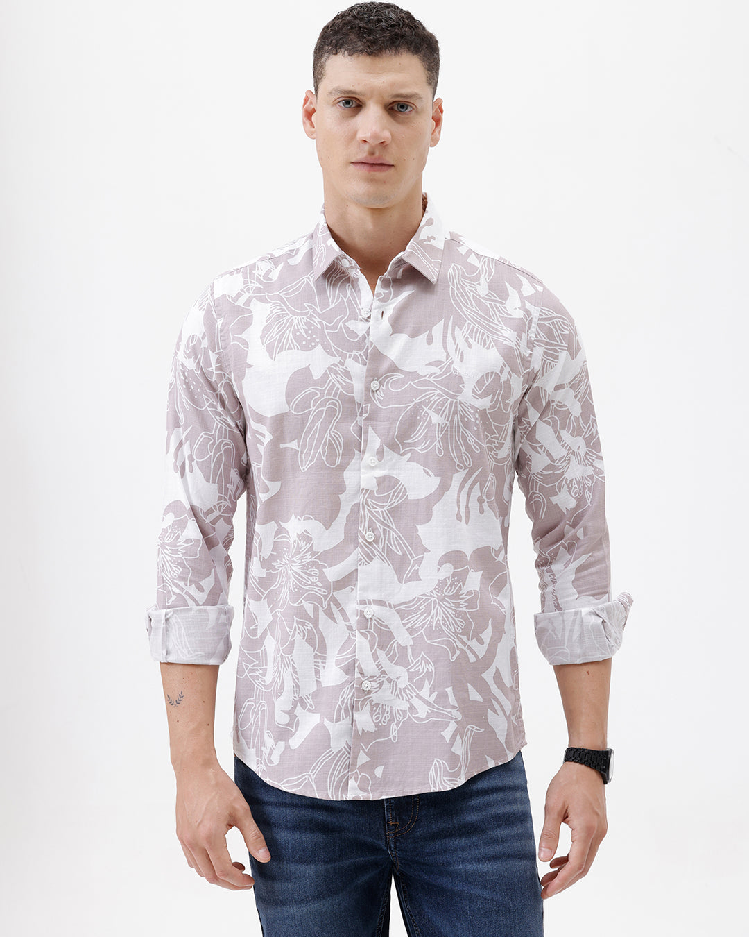A man wearing a long-sleeve button-up shirt with a light gray and white abstract floral pattern, paired with dark blue jeans, standing against a plain white background.