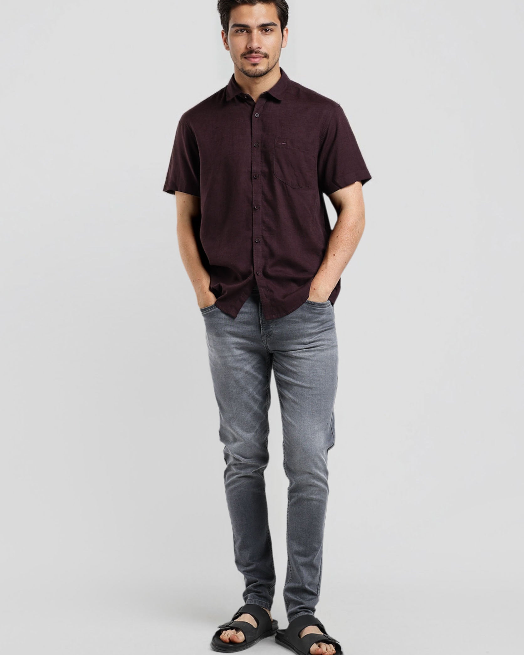 Man wearing a dark brown shirt and gray pants on a light gray background