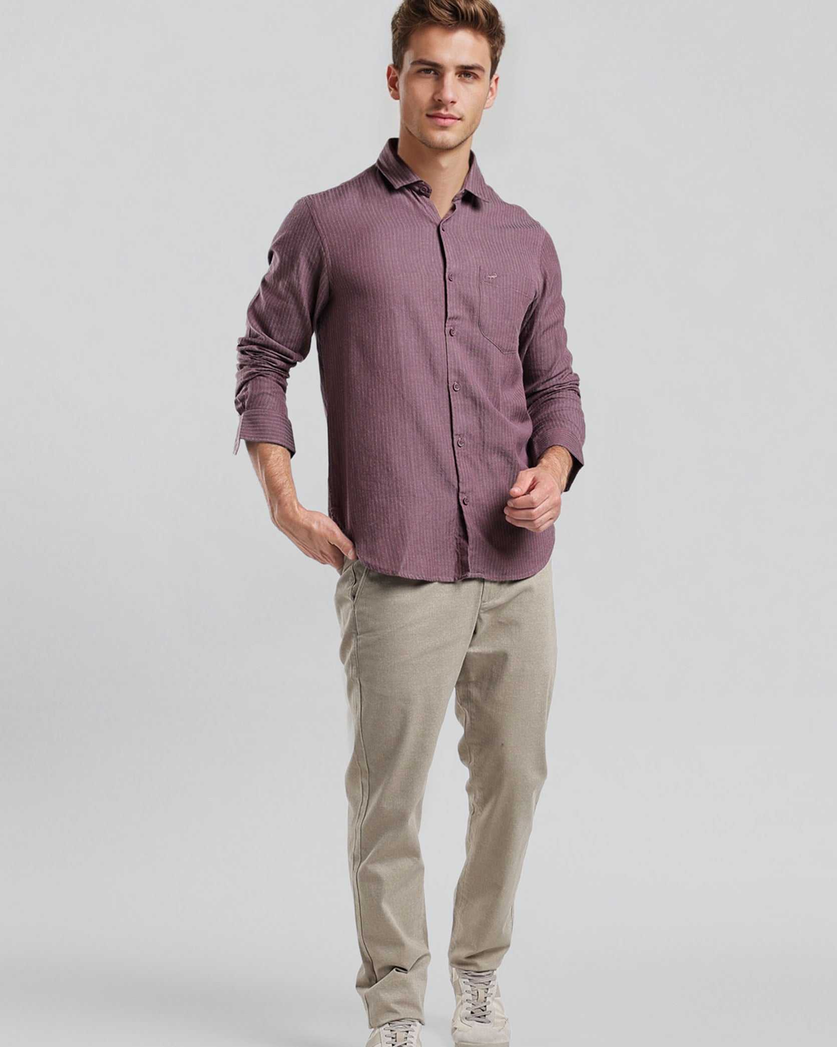 Man wearing a purple shirt and beige pants on a light gray background