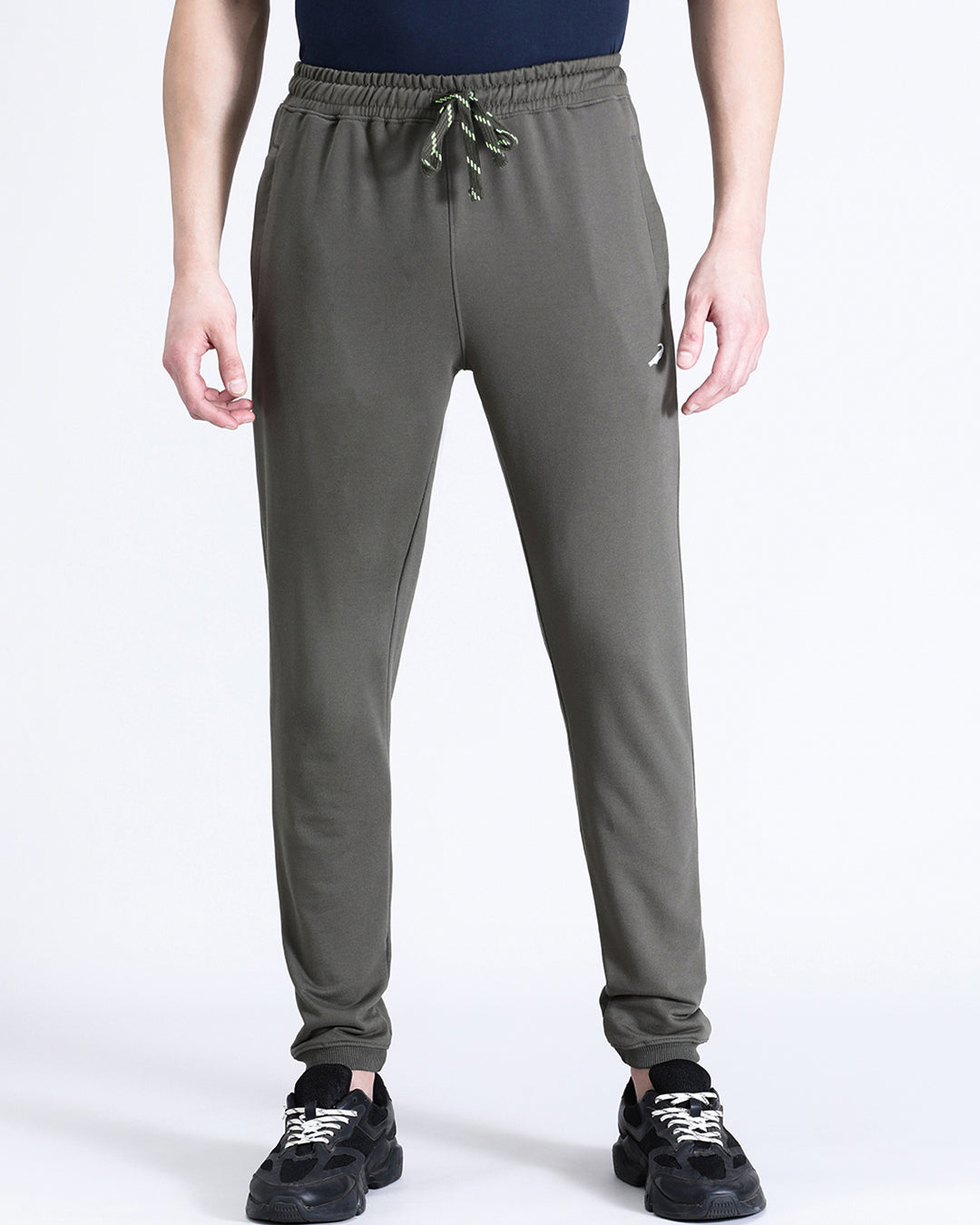 A person standing wearing dark olive green comfort fit joggers with a drawstring waist, paired with a navy top and black sneakers.