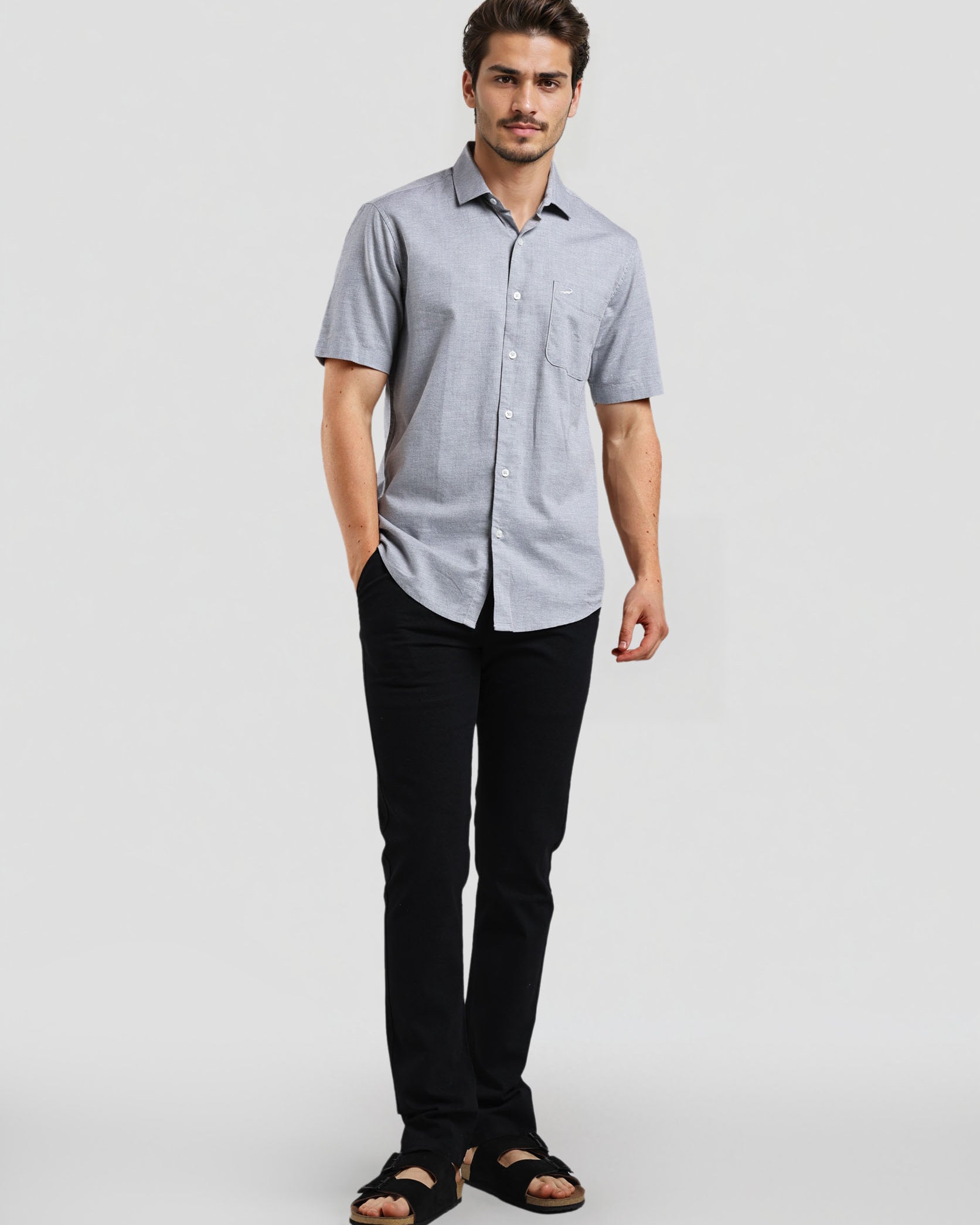 Man wearing a light gray short-sleeve shirt and black pants on a white background