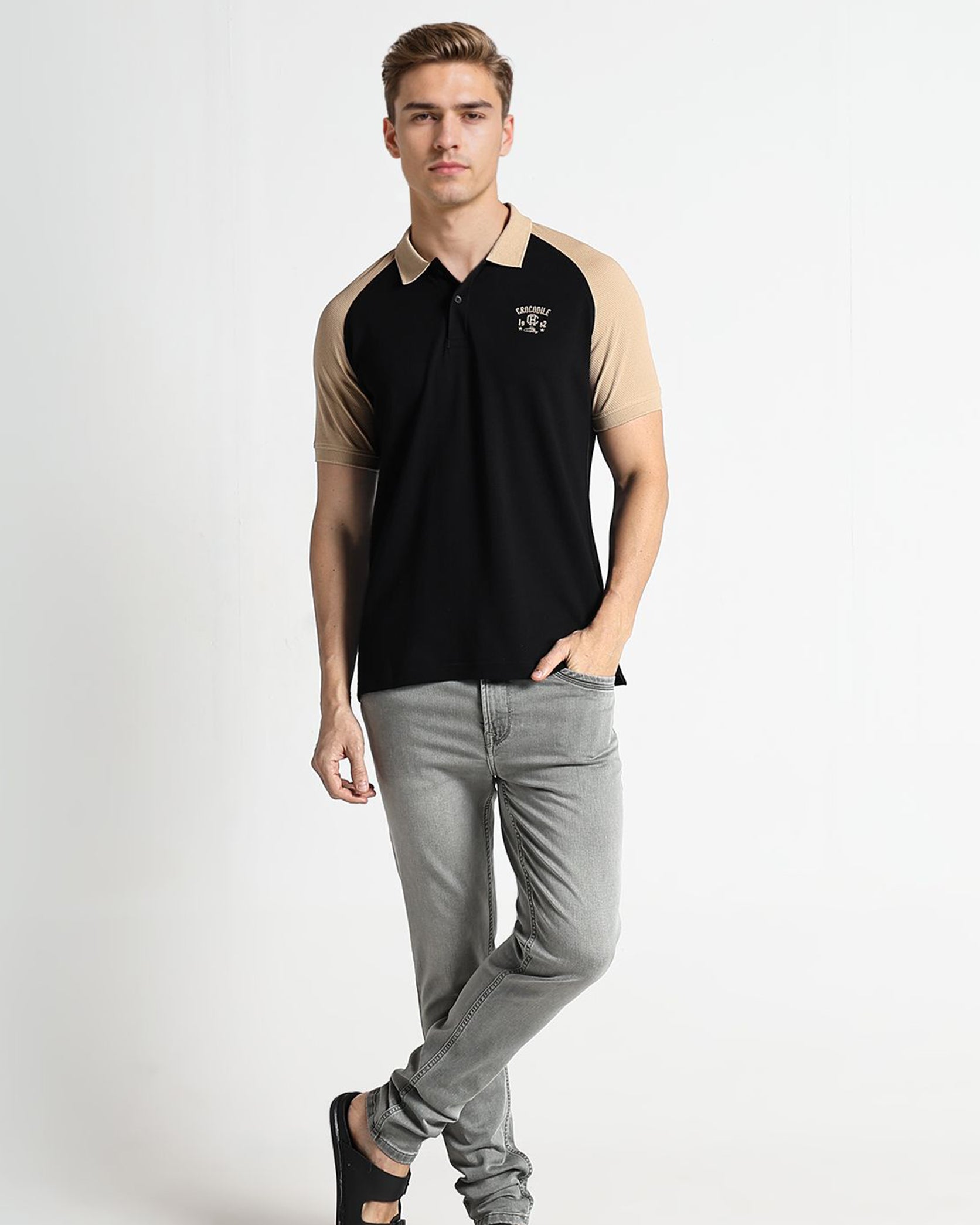 Man wearing a black and beige polo shirt with gray pants on a white background