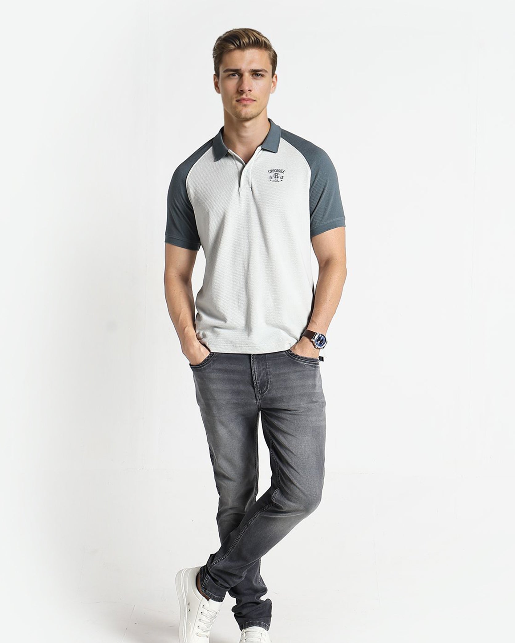 Man wearing a white and gray polo shirt with dark gray pants on a white background