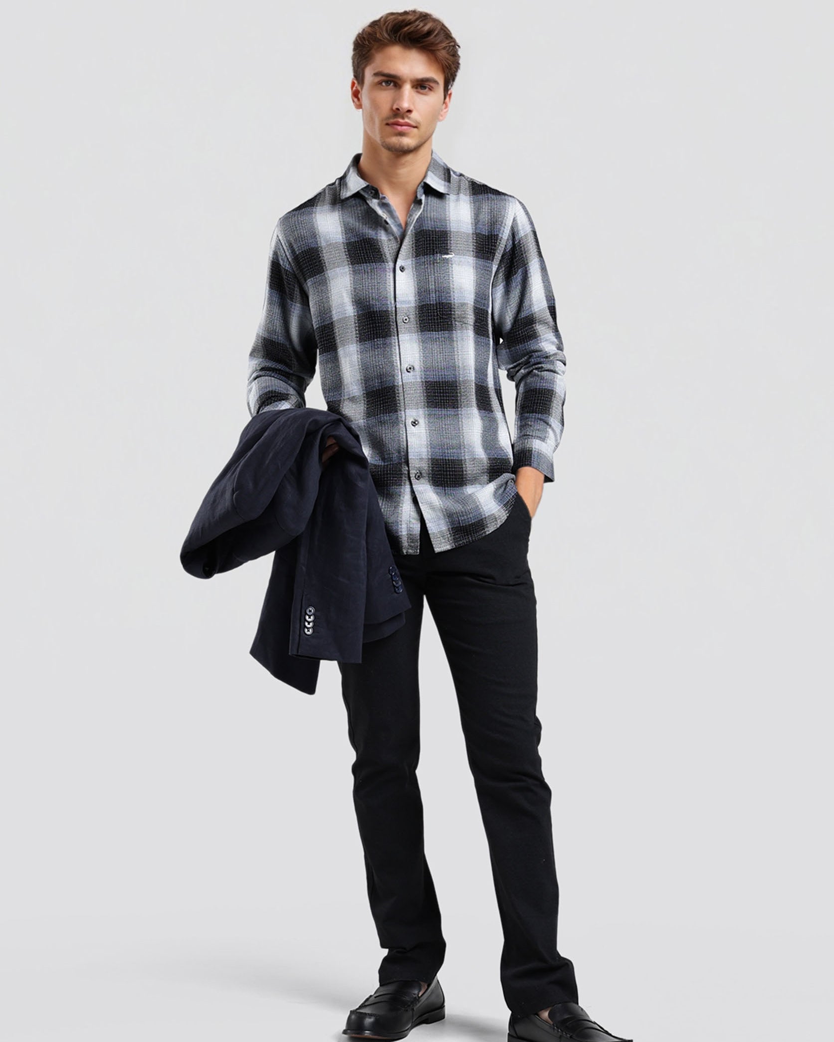 Man wearing a plaid shirt, black jacket, and black pants on a light gray background