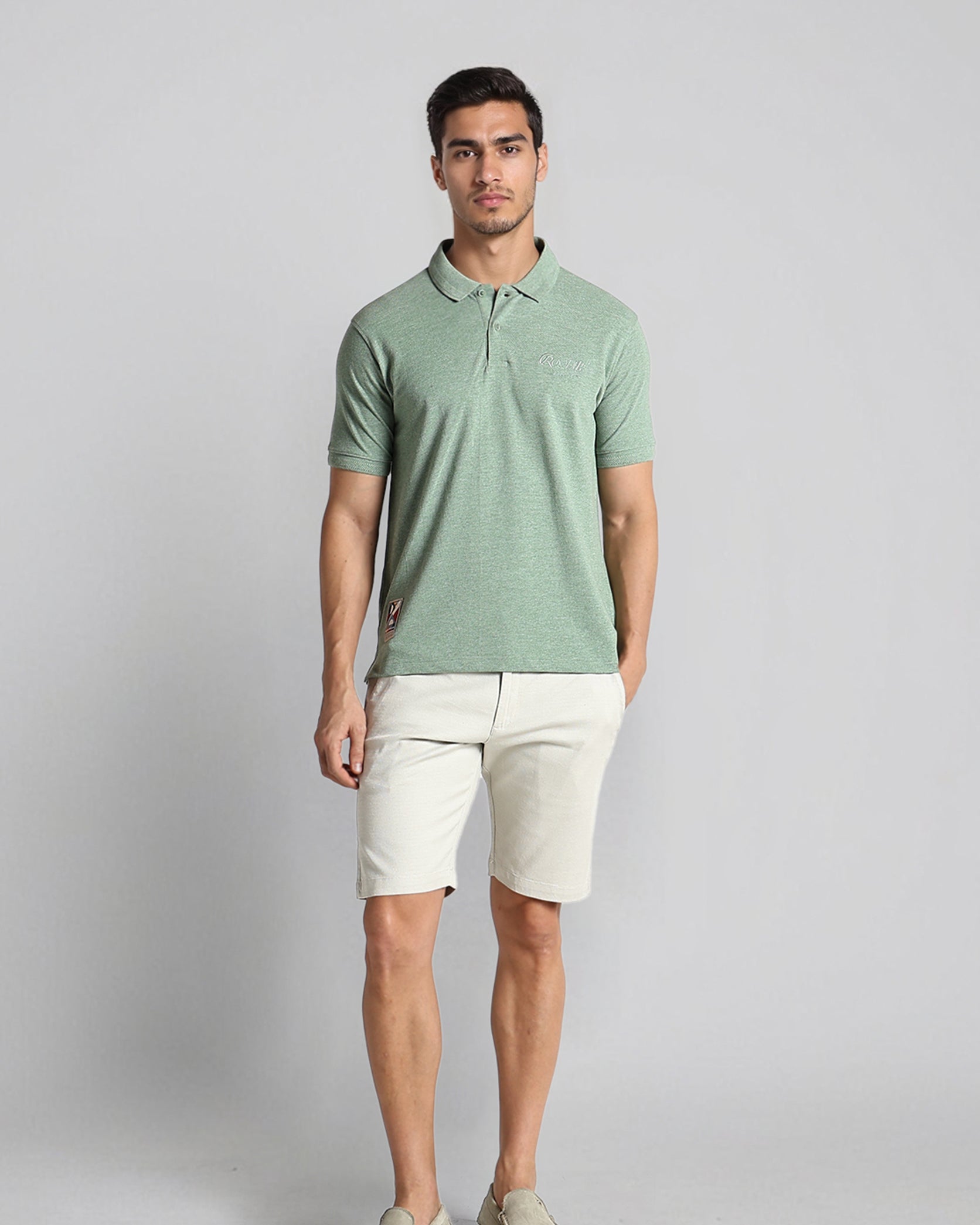 Man wearing a green polo shirt and beige shorts against a gray background