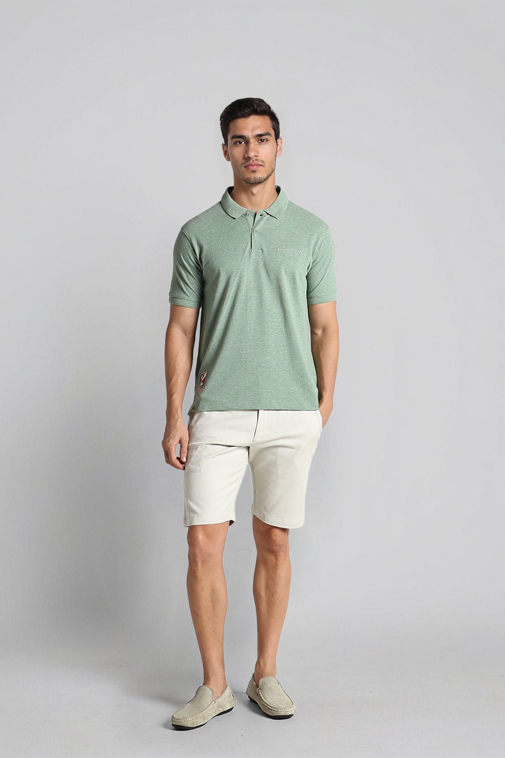 Man wearing a green polo shirt and beige shorts against a gray background