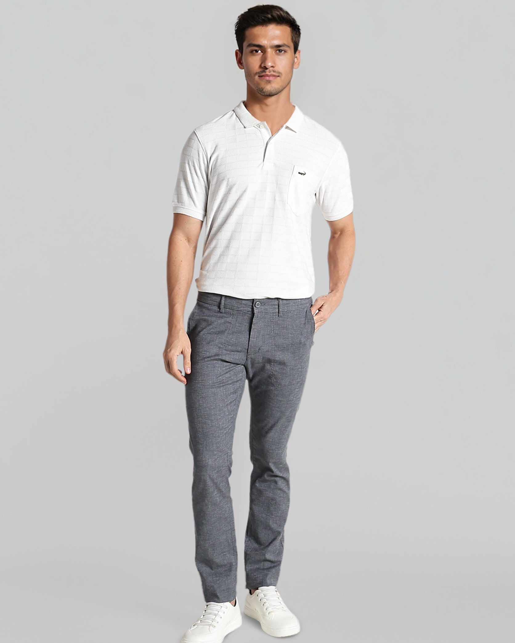 Man wearing a white polo shirt and gray pants on a gray background