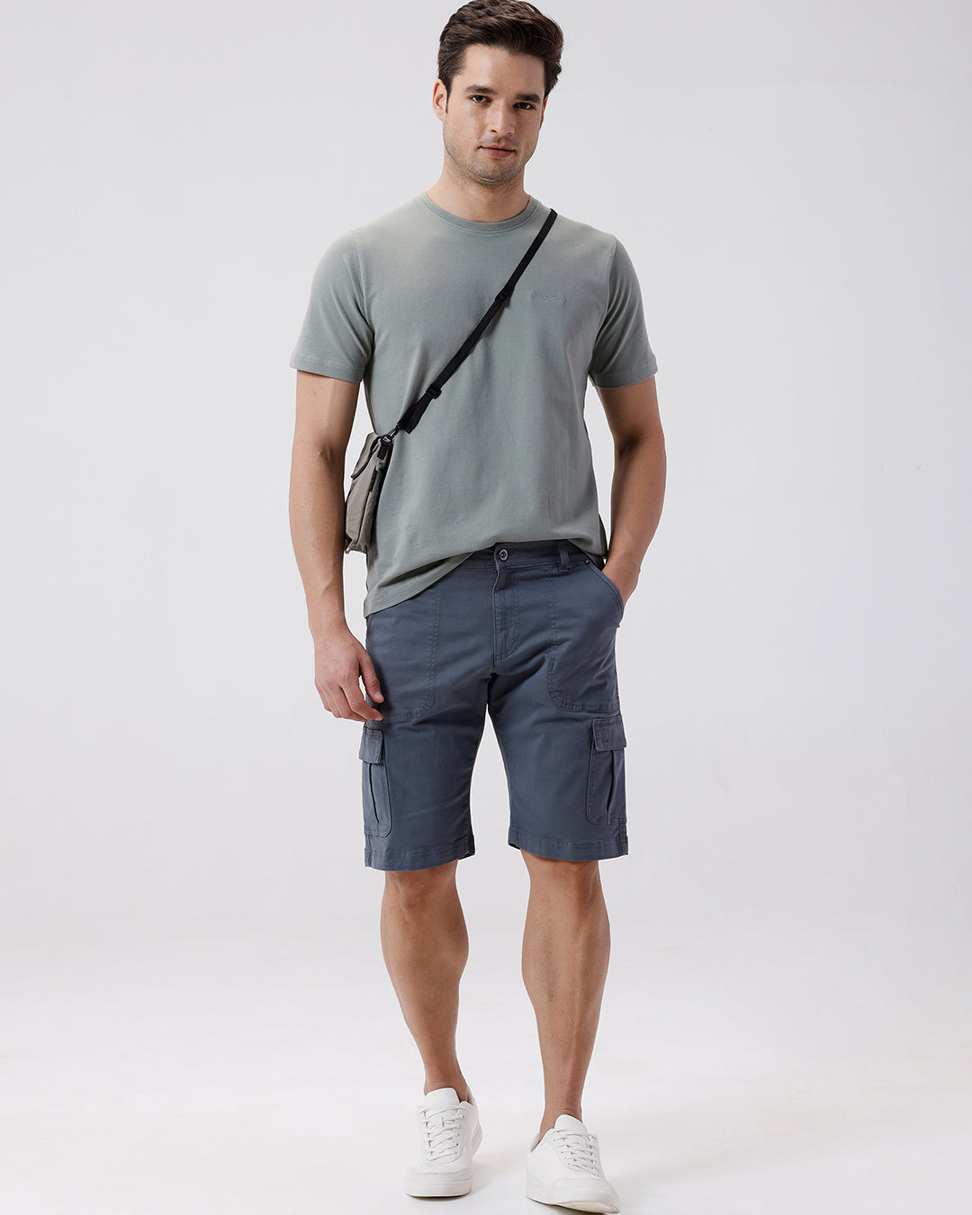 Man wearing a grey garment dyed cargo shorts in dark grey with casual styling on a gray background