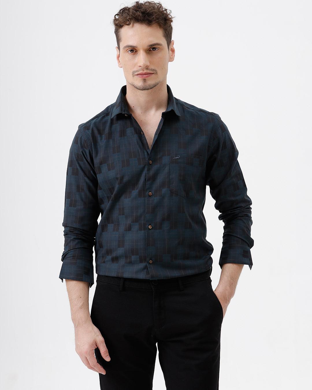 A man wearing a dark navy blue patterned long-sleeve button-up shirt and black trousers, standing against a plain white studio background.