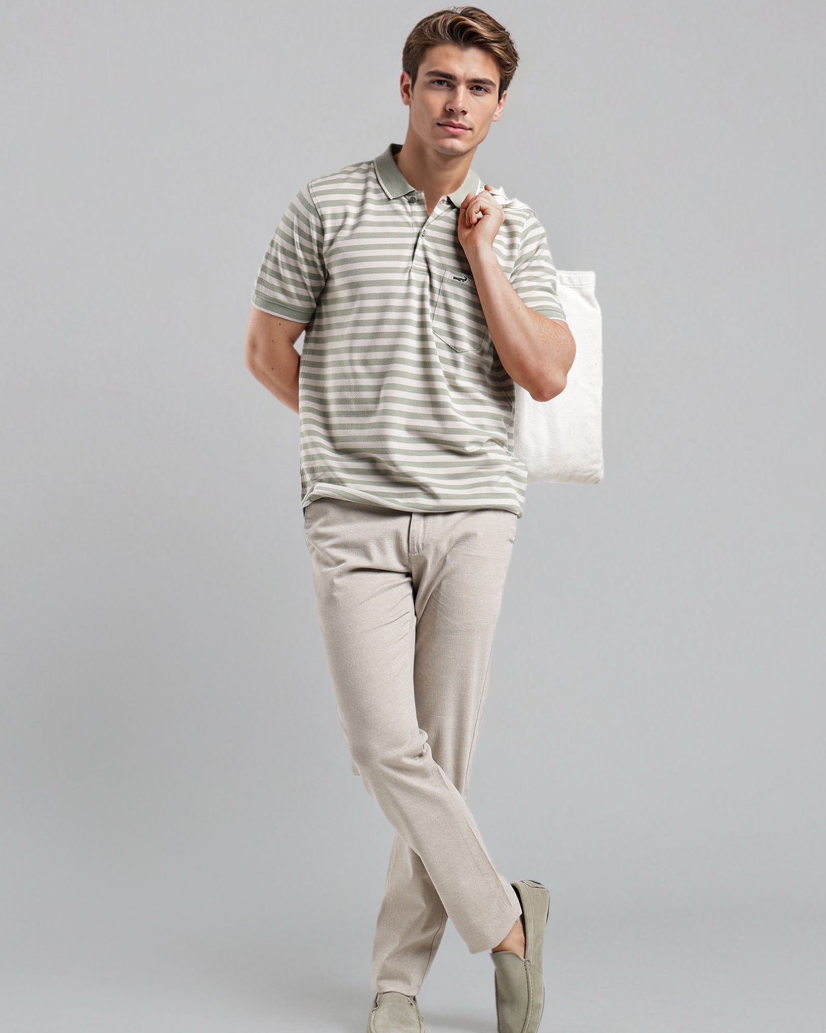 Man wearing a striped polo shirt and beige pants holding a white bag on a gray background