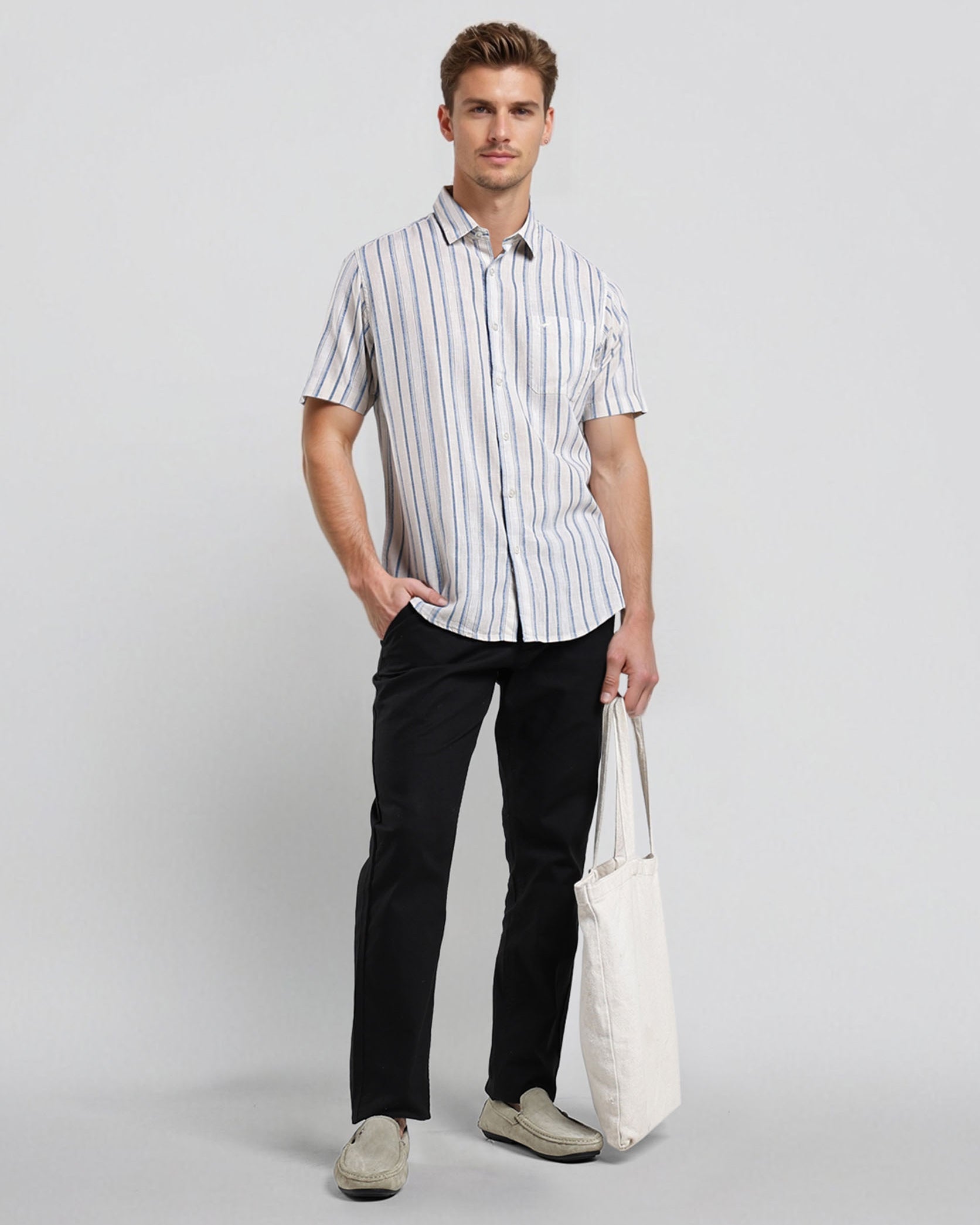 Man wearing a striped shirt and black pants holding a white bag on a light gray background