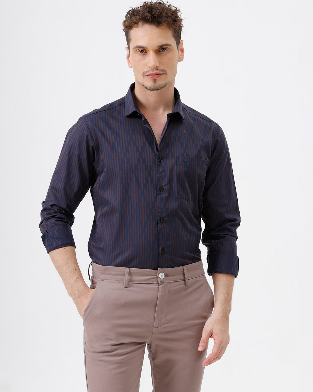 A man wearing a dark navy blue button-down shirt with thin vertical red stripes and light brown trousers, standing against a plain white studio background.
