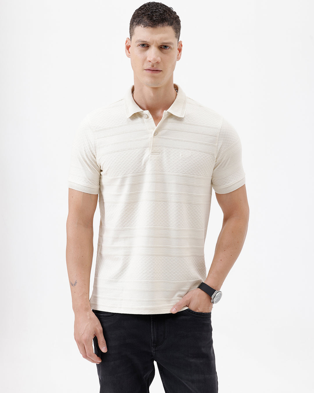 A man wearing a short-sleeve polo shirt in cream with subtle horizontal textured stripes, paired with dark jeans, standing against a plain white studio background.