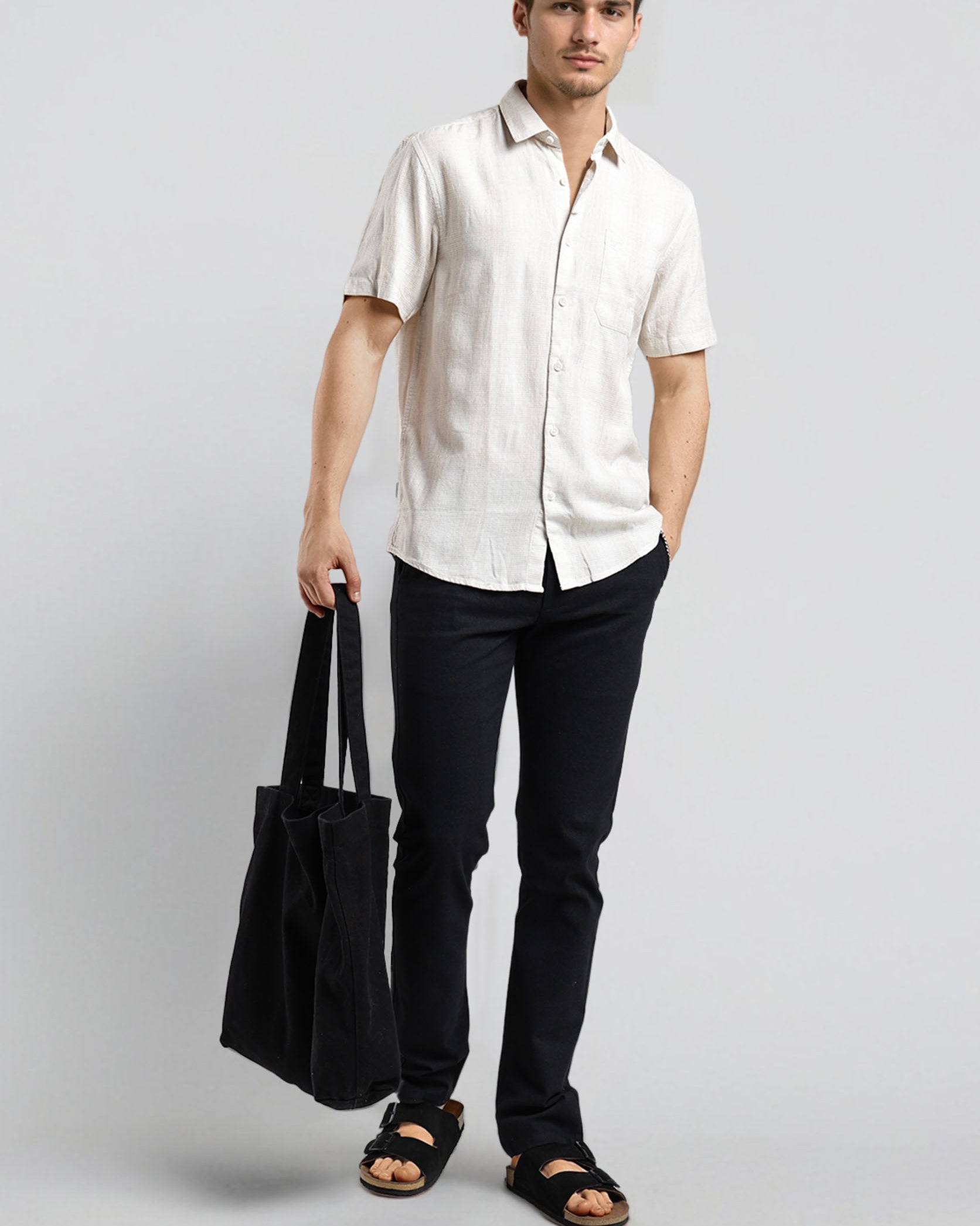 Man wearing a white shirt and black pants holding a black bag on a gray background