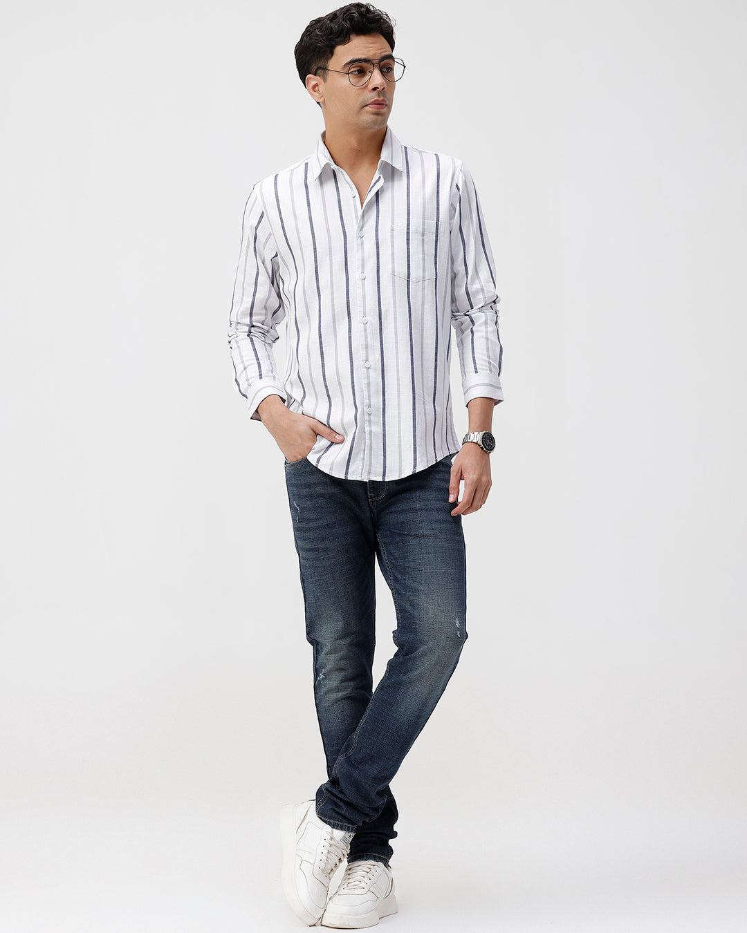 Man wearing a striped shirt, jeans, and white sneakers on a white background