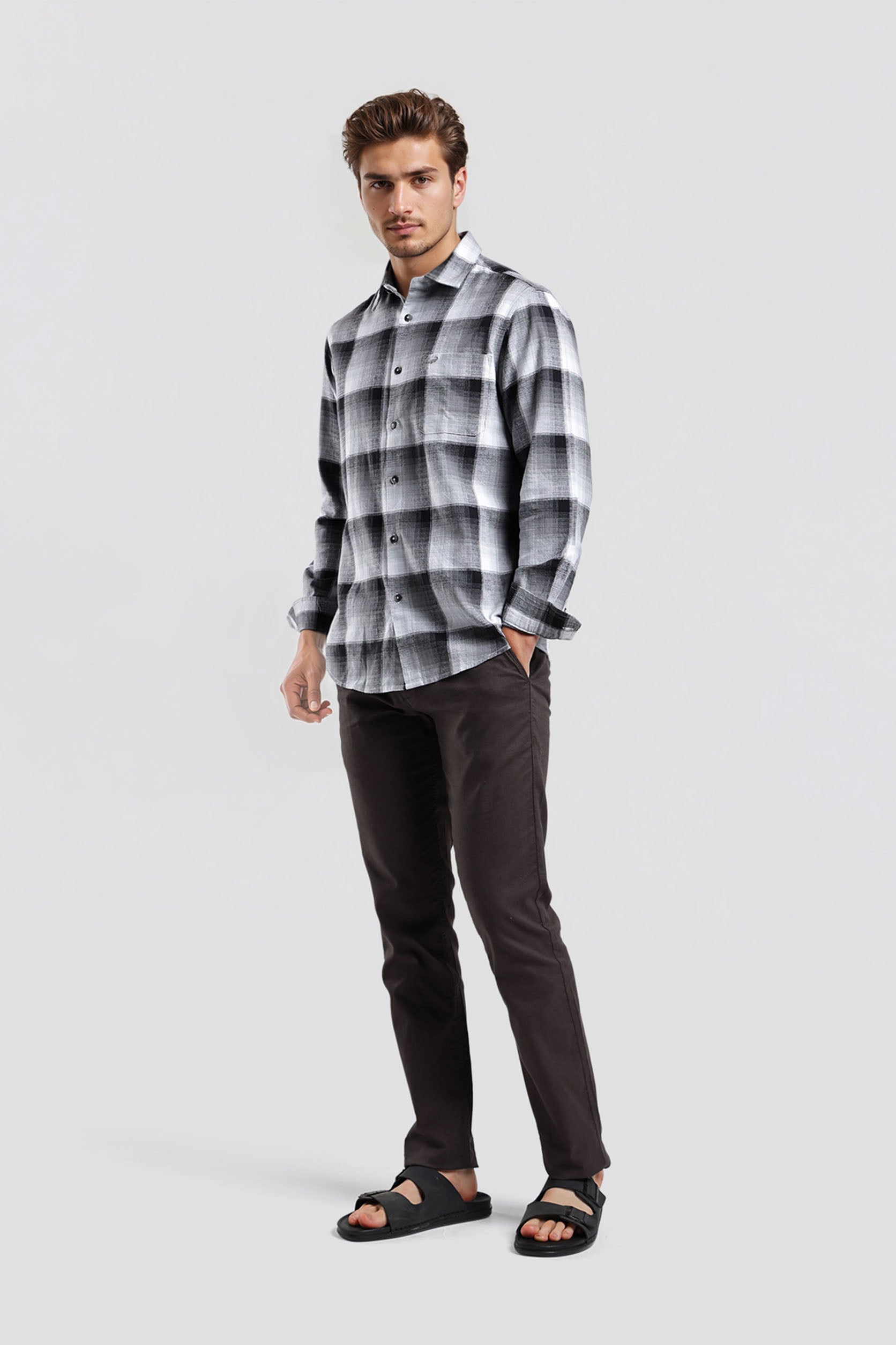 Man wearing a plaid shirt and dark pants on a white background