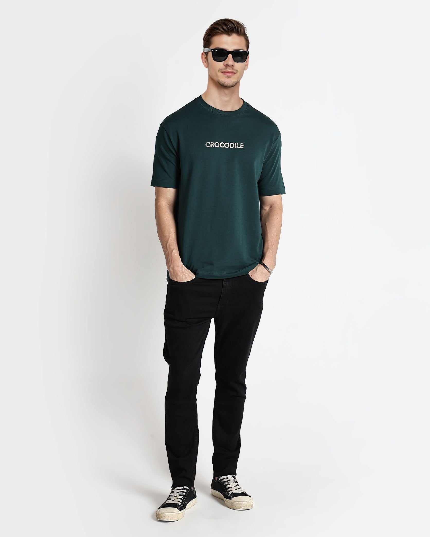 Man wearing a green t-shirt with 'Crocodile' logo and black pants on a white background