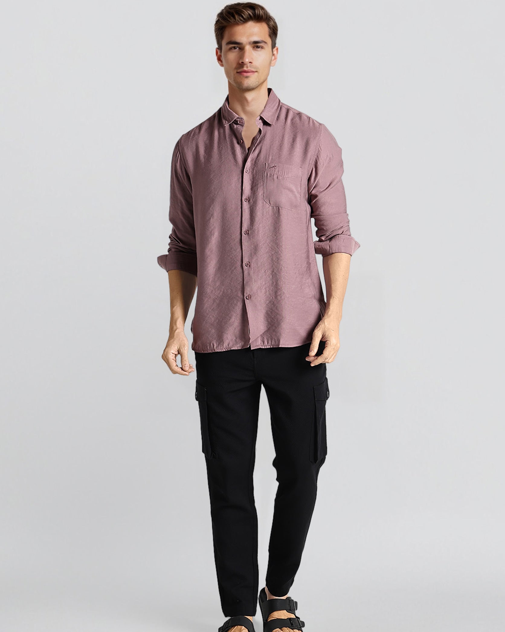 Man wearing a mauve button-up shirt and black pants on a light gray background