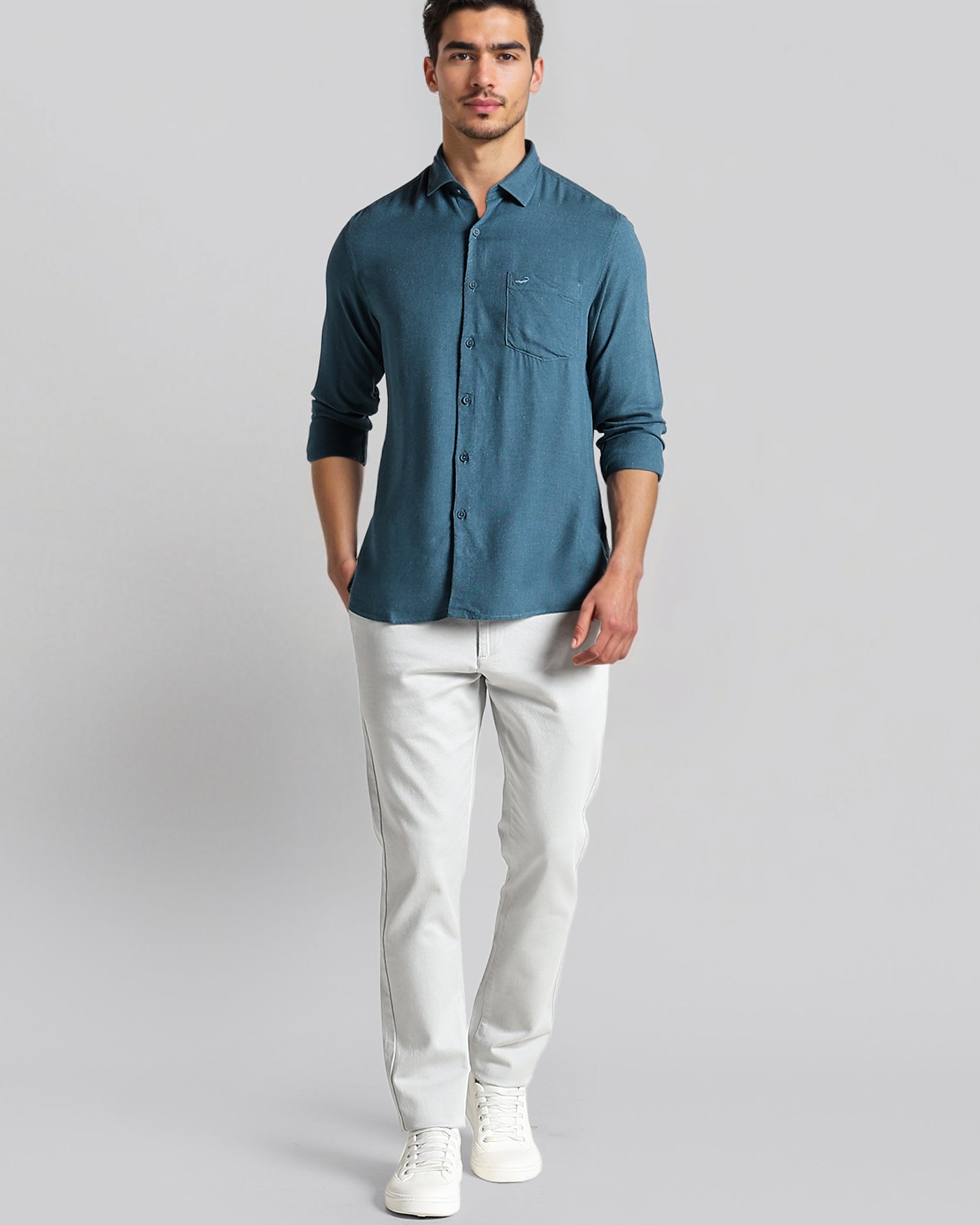 Man wearing a blue shirt and white pants on a gray background