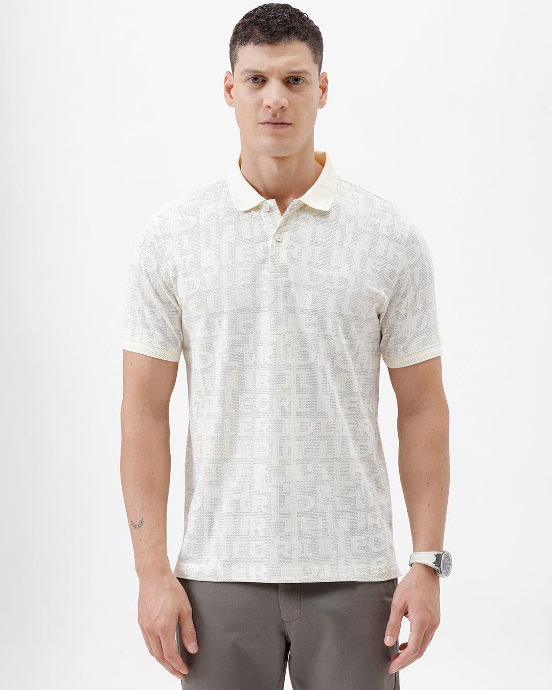 A man wearing a short-sleeve polo shirt with a subtle repeating monogram pattern in cream and light gray, paired with gray trousers, photographed against a plain white studio background.
