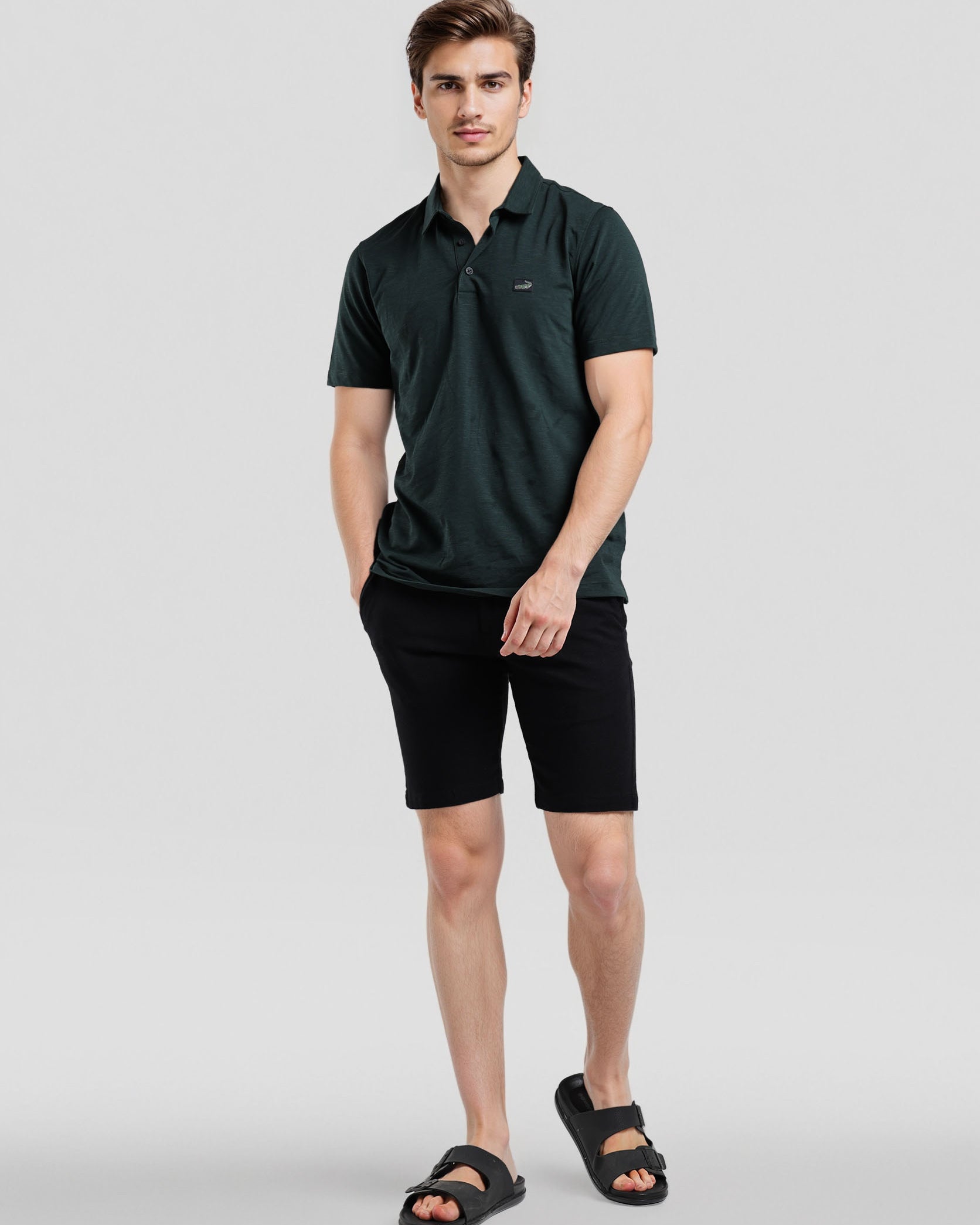 Man wearing a dark green polo shirt and black shorts on a light gray background