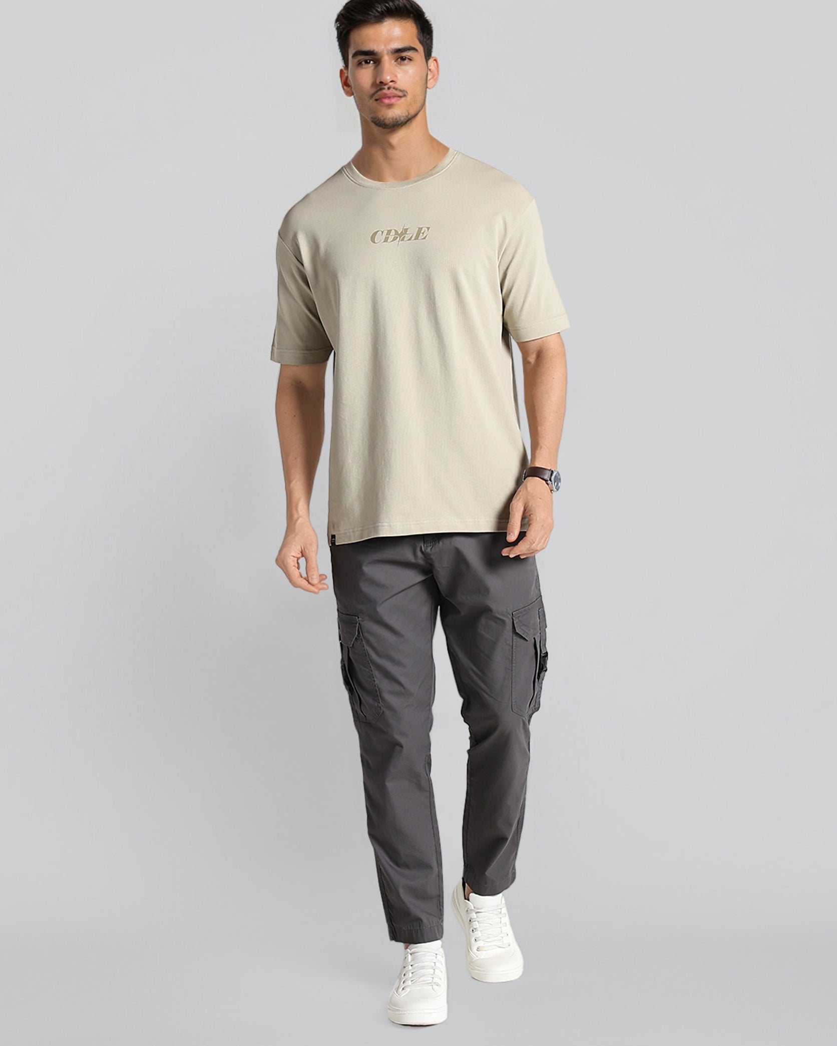 Man wearing a beige t-shirt and gray cargo pants on a light gray background