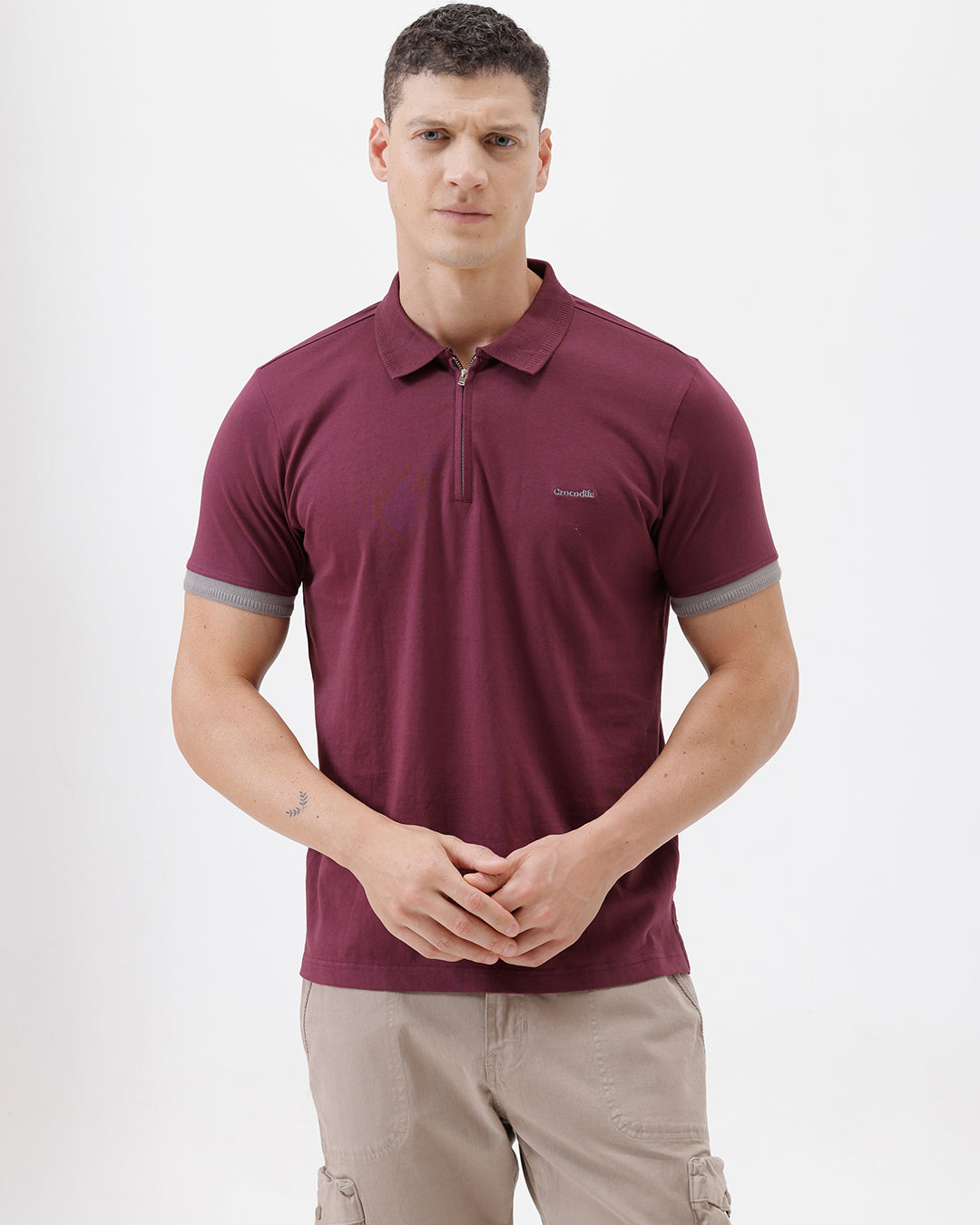 A man wearing a short-sleeve polo shirt in maroon with gray sleeve trim and a half-zip collar, paired with beige cargo pants, against a plain white studio background.