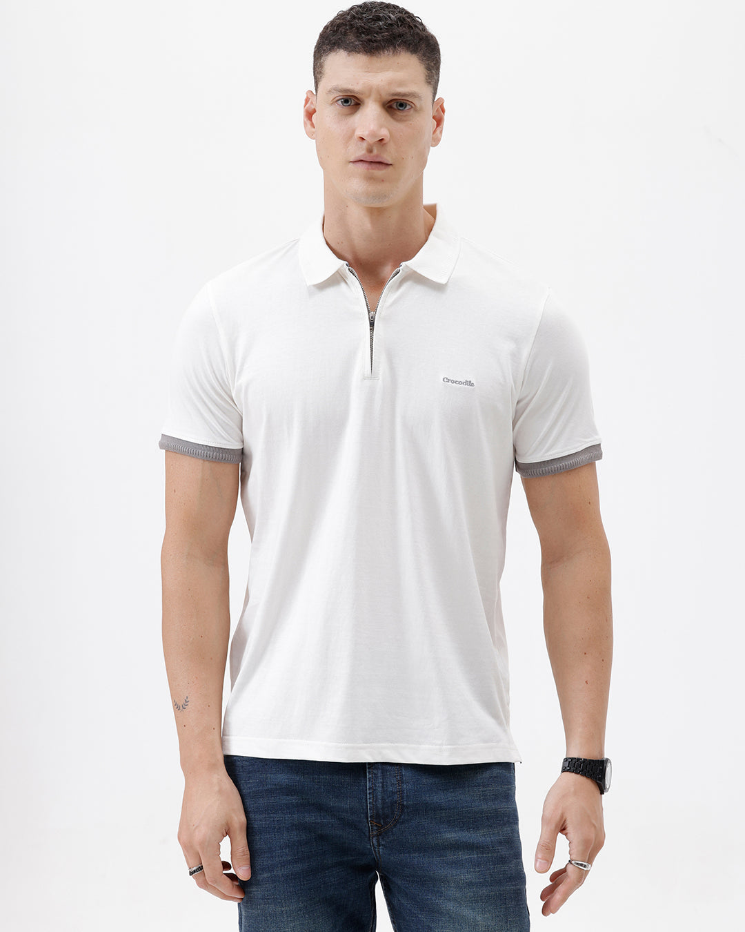 A man wearing a white short-sleeve polo shirt with gray ribbed trim on the collar and sleeve cuffs, paired with dark blue jeans, photographed against a plain white studio background.