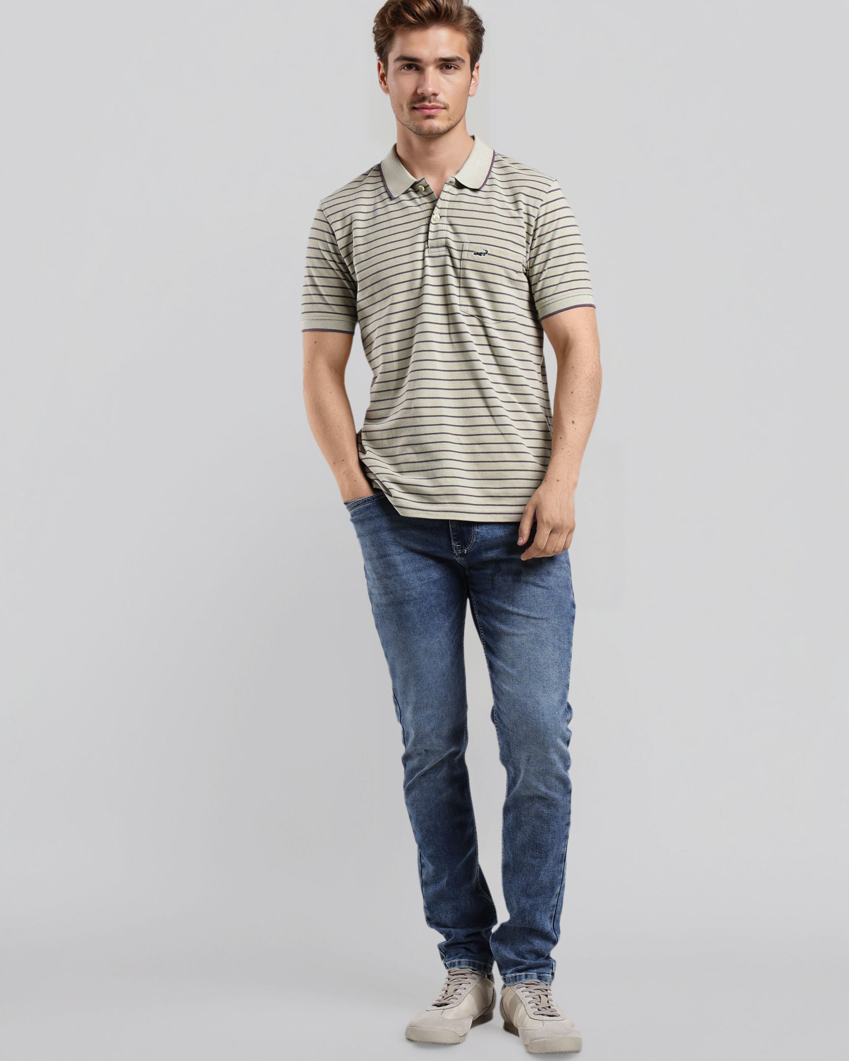 Man wearing a striped polo shirt and blue jeans on a gray background