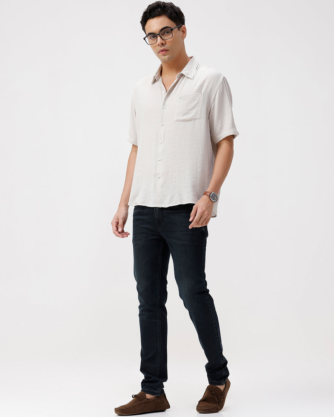 Man wearing a light-colored shirt, dark jeans, and brown shoes on a white background