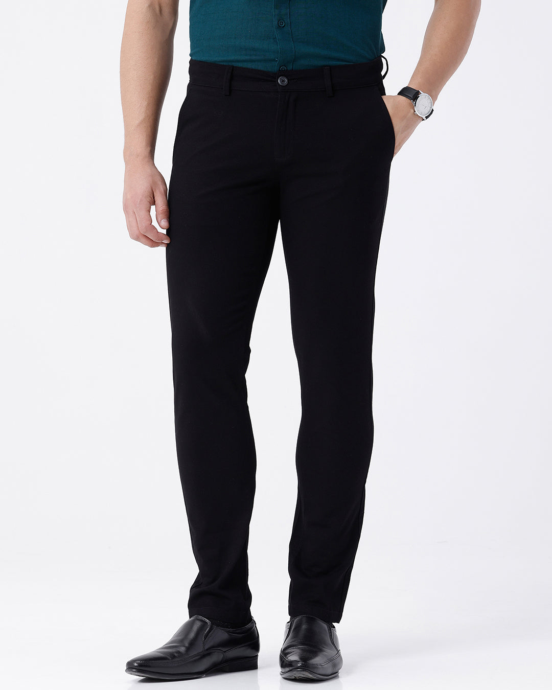 A man wearing slim-fit black trousers, a teal button-down shirt, and black leather dress shoes, standing against a plain white studio background.