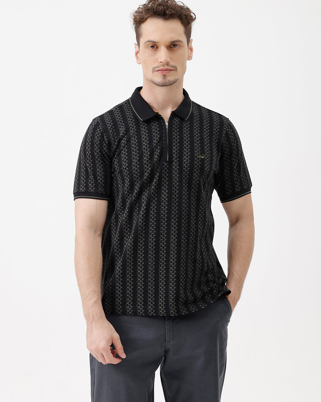 A man wearing a black short-sleeve polo shirt with a subtle geometric pattern, paired with dark gray trousers, standing against a plain white studio background.
