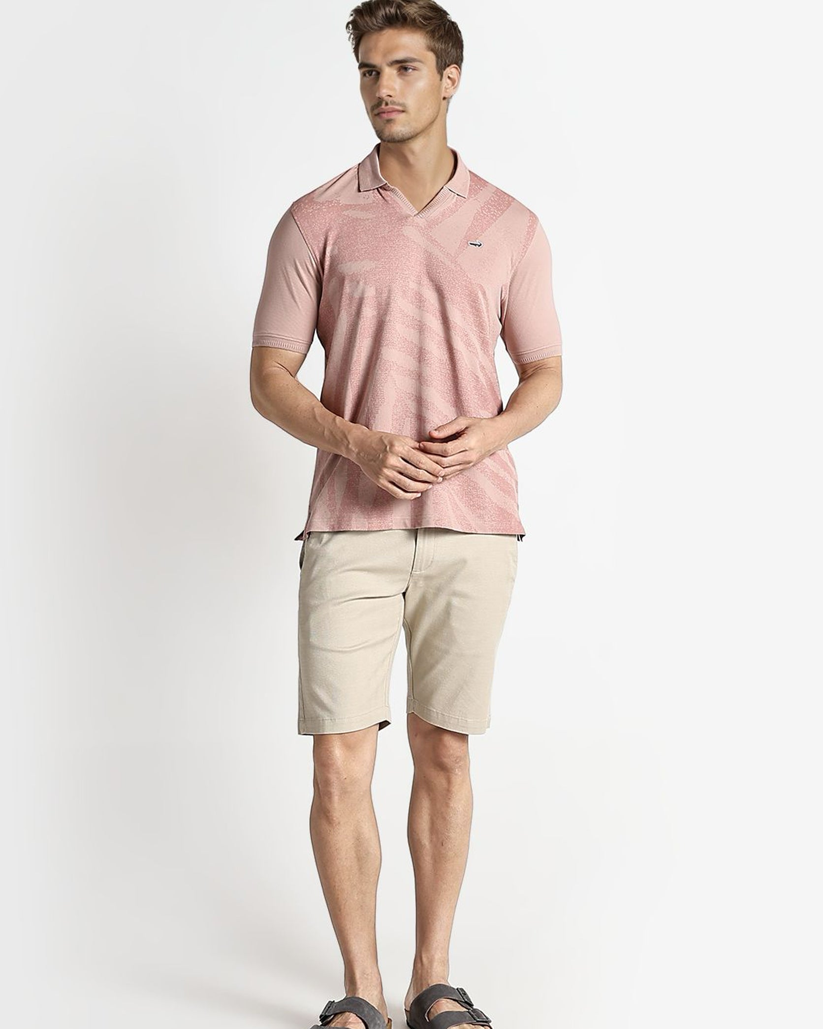 Man wearing a pink polo shirt and beige shorts on a white background
