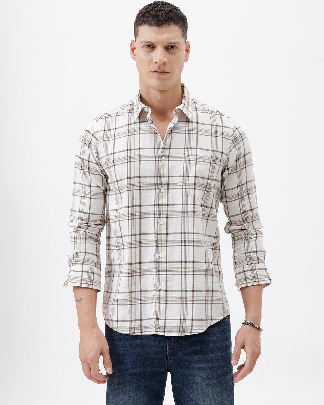 A man wearing a long-sleeve plaid button-up shirt in beige and brown with dark blue jeans, standing against a plain white studio background.