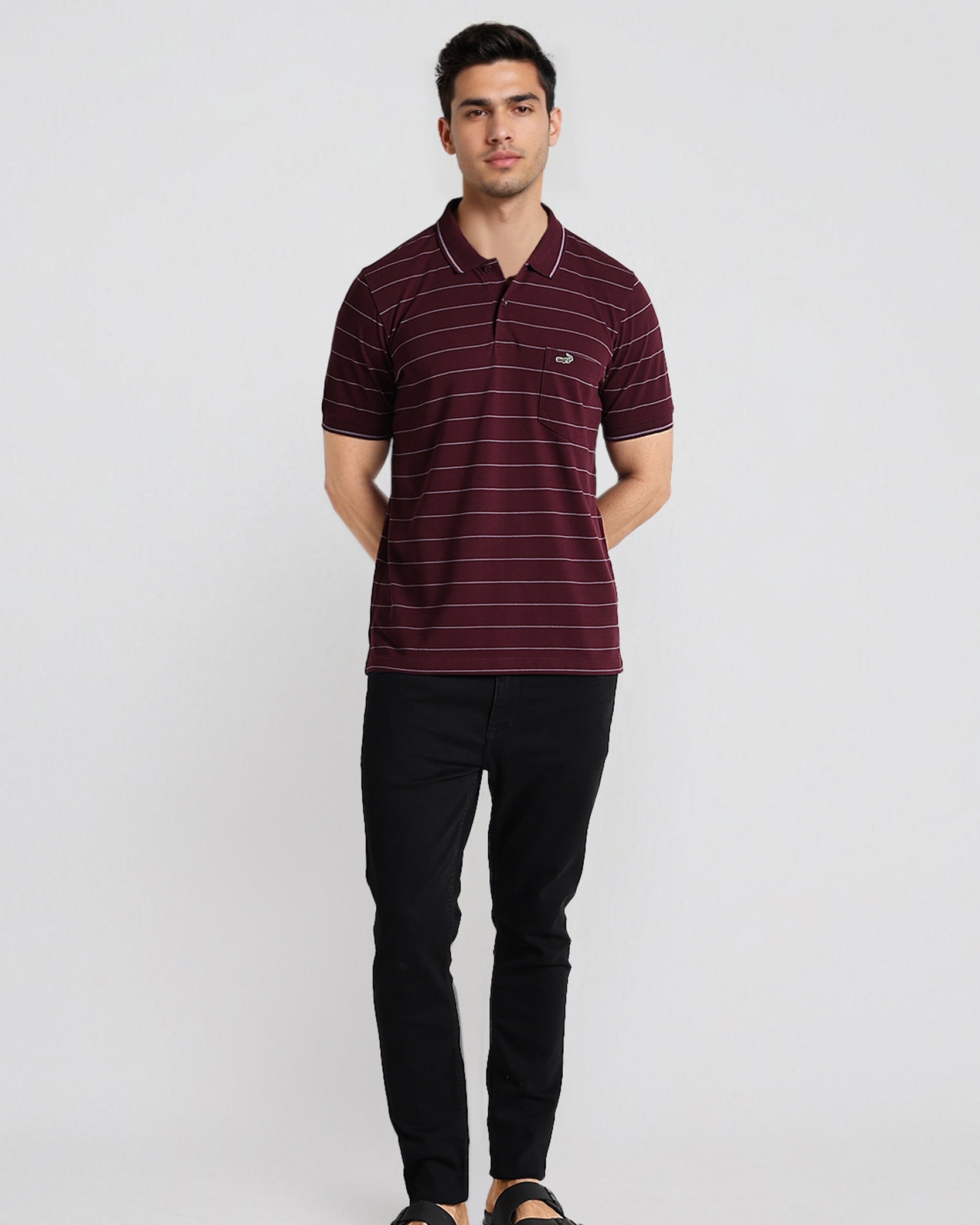 Man wearing a maroon striped polo shirt and black pants on a white background