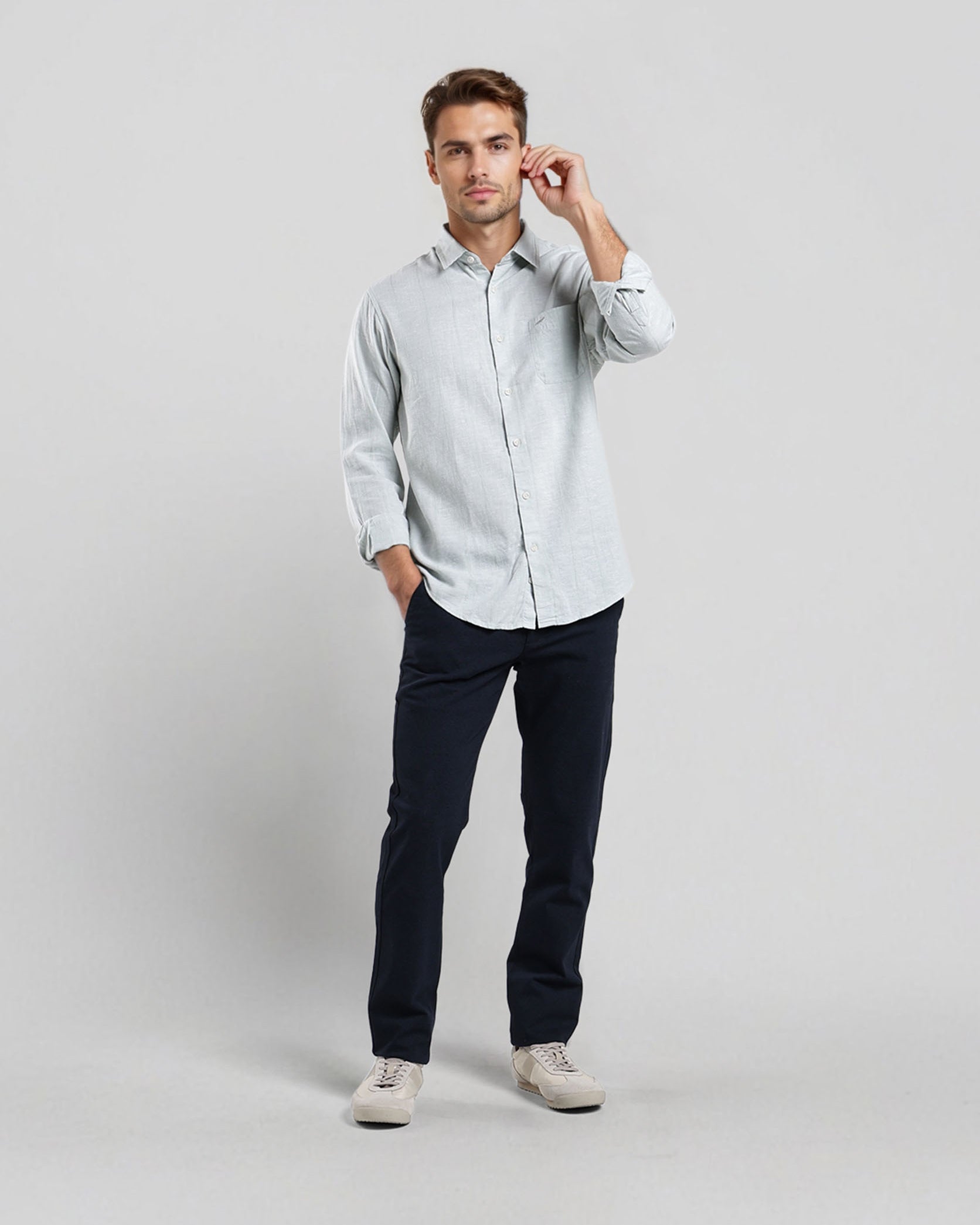 Man wearing a light gray button-up shirt and dark pants on a white background