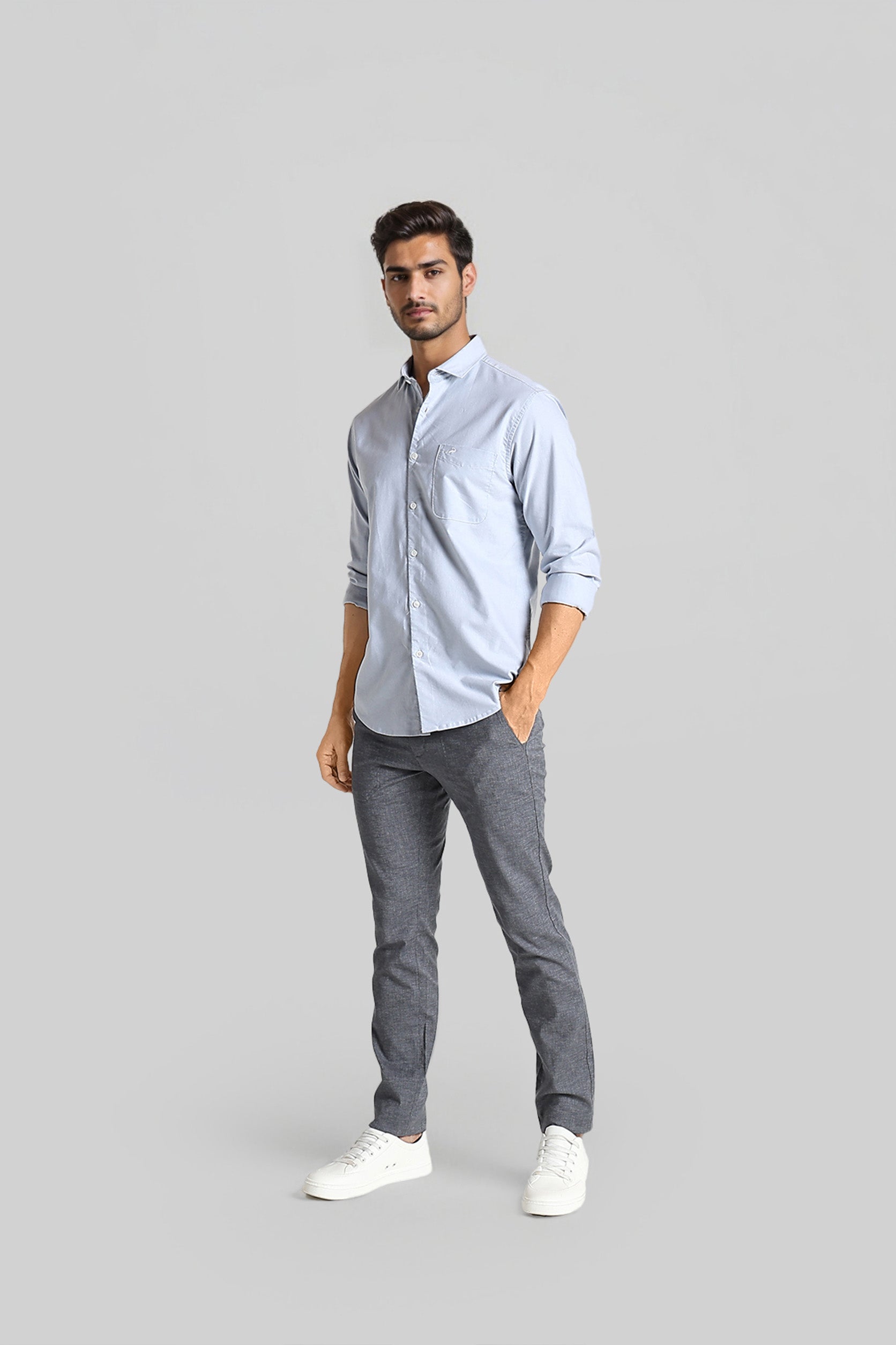 Man wearing a light blue shirt and gray pants on a gray background