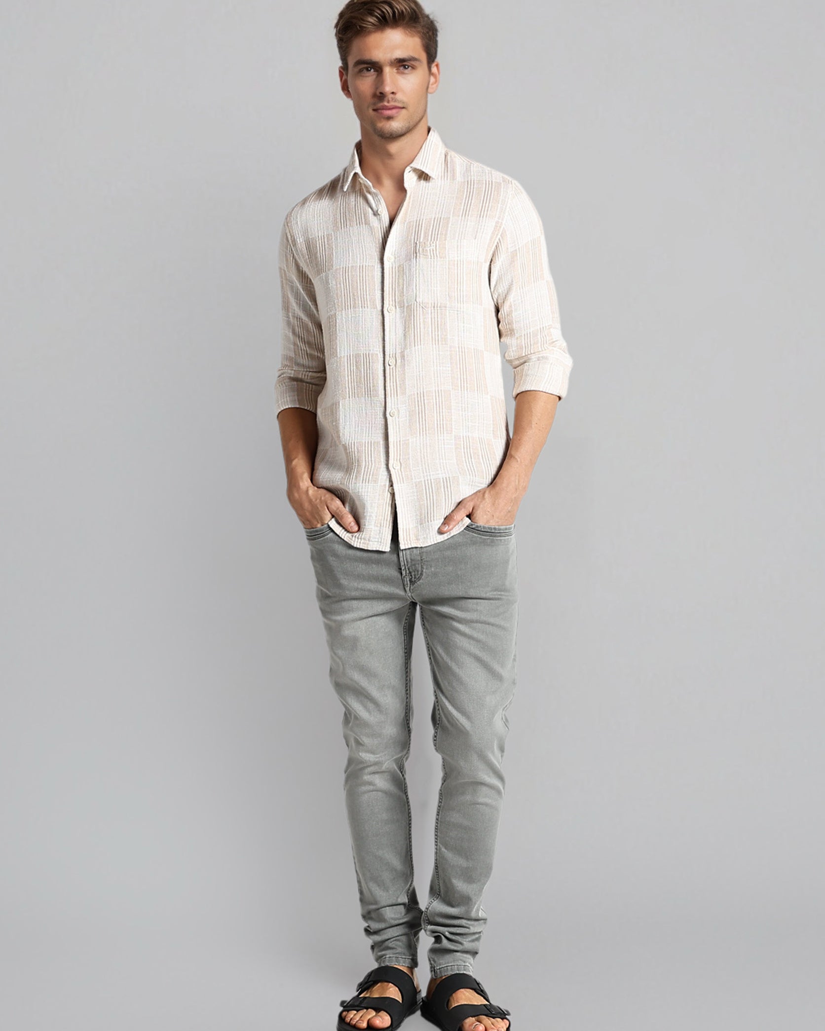 Man wearing a light-colored shirt and gray pants on a gray background