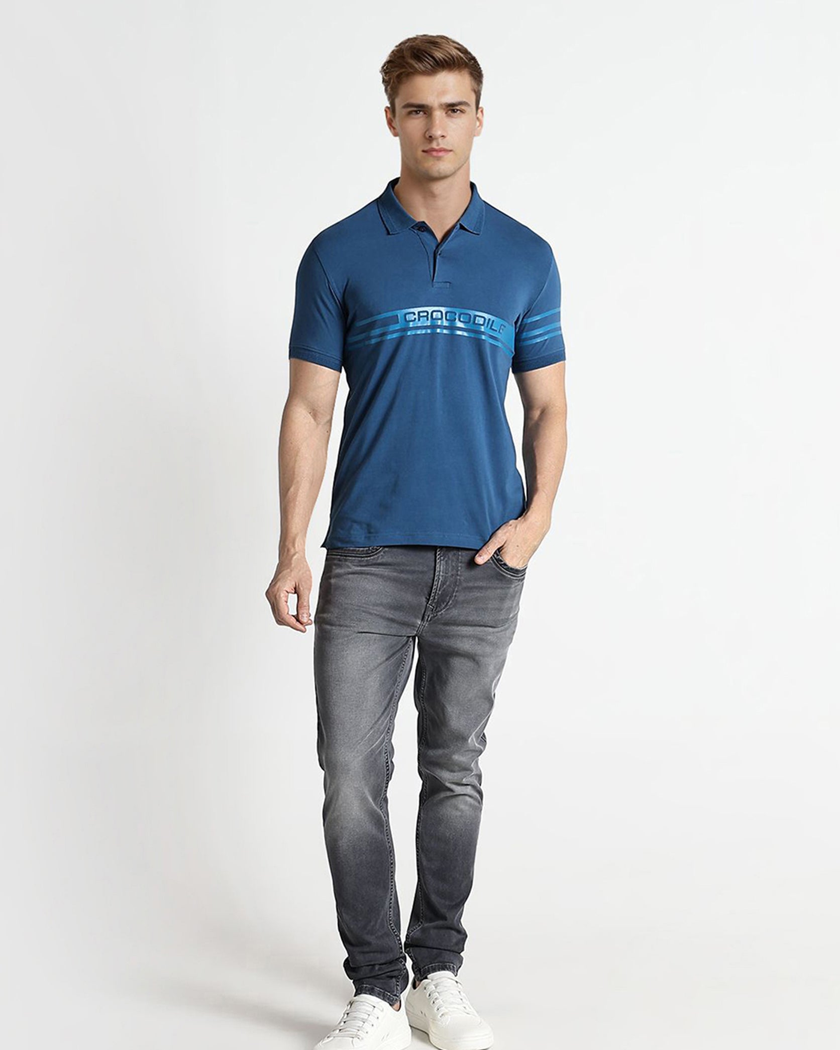 Man wearing a blue polo shirt and gray jeans on a white background