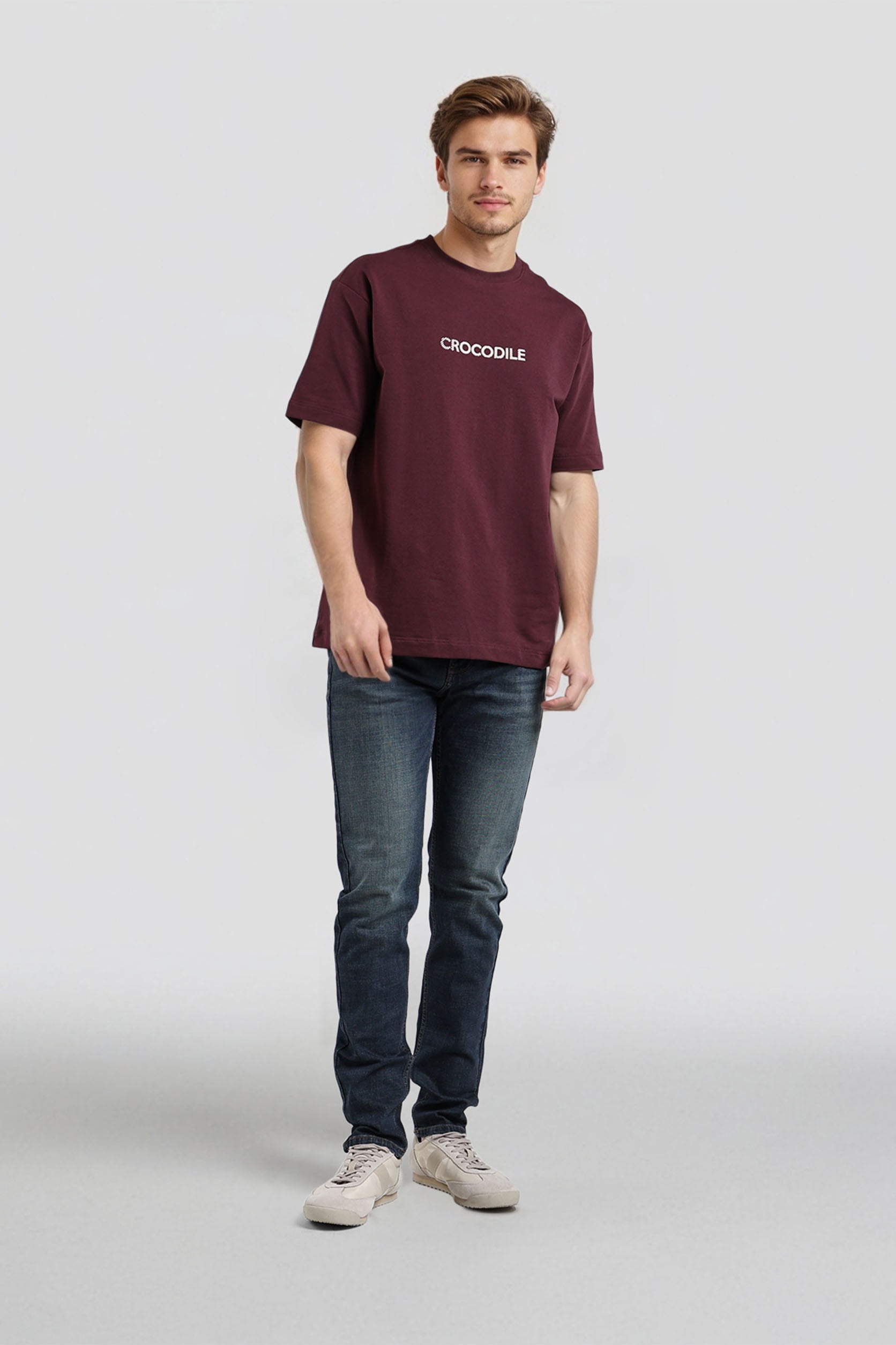 Man wearing a maroon t-shirt with 'Crocodile' logo and dark jeans on a white background