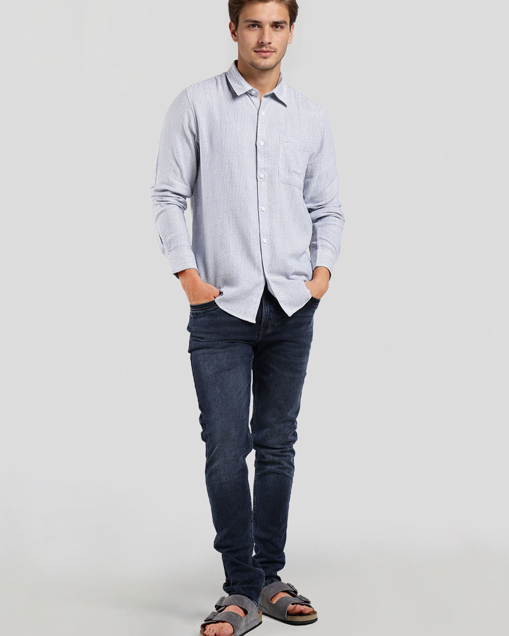 Man wearing a light blue button-up shirt and dark jeans on a white background