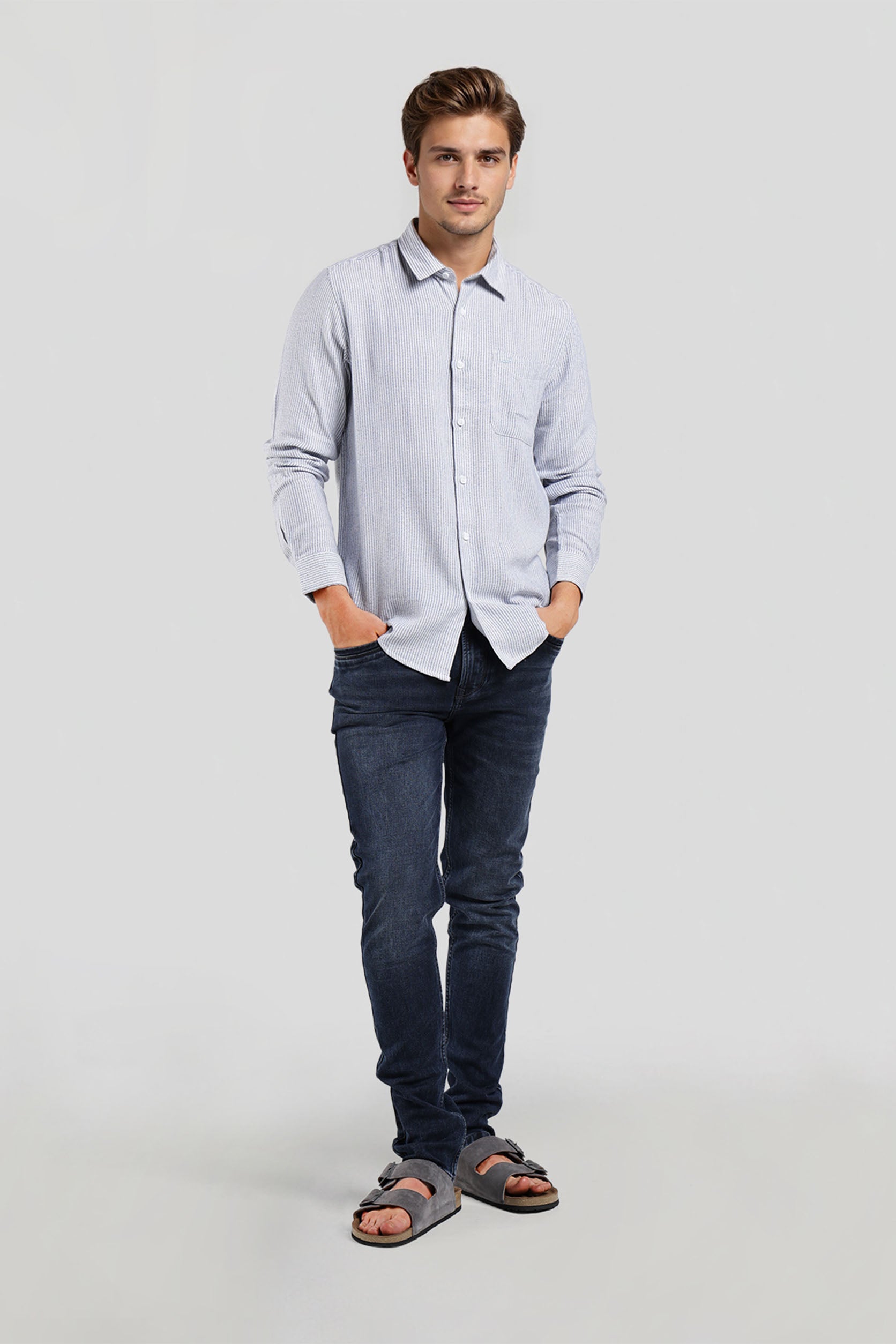 Man wearing a light blue button-up shirt and dark jeans on a white background
